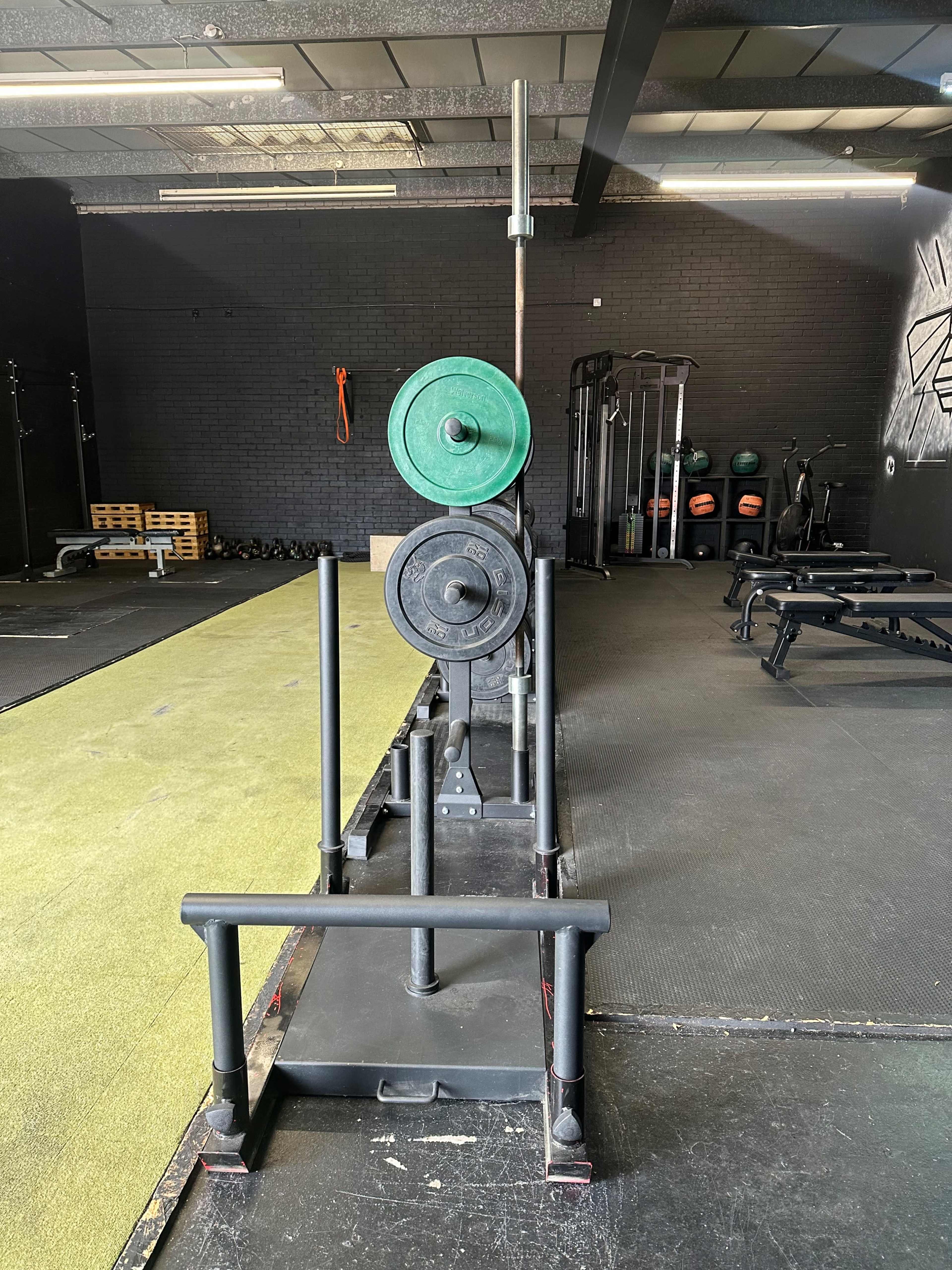 A weightlifting sled with green and black weights in an empty gym environment.
