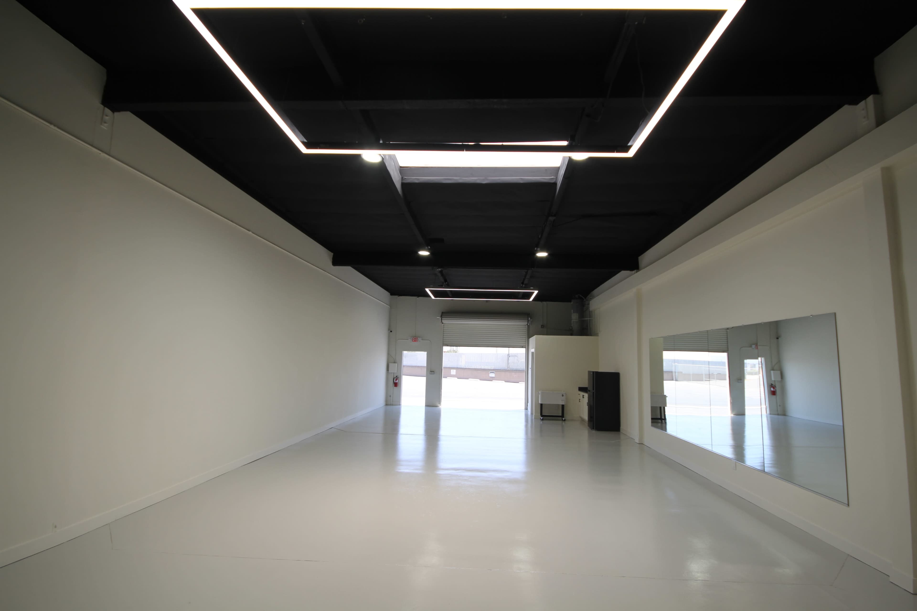 An empty interior space with white walls, a glossy white floor, and modern overhead lighting.