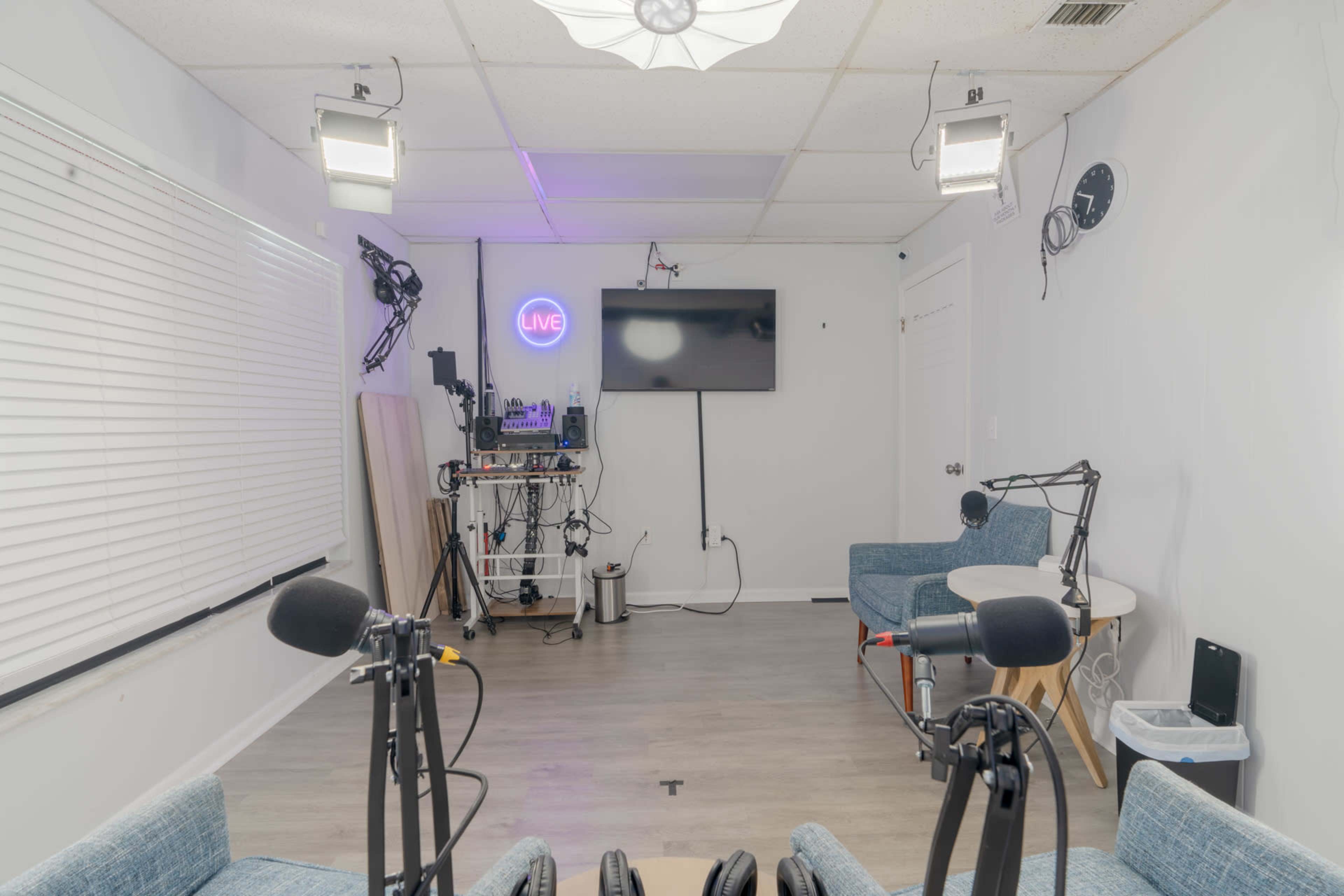 A modern room set up for a live recording, featuring two chairs, a table, microphones, and a television mounted on the wall.