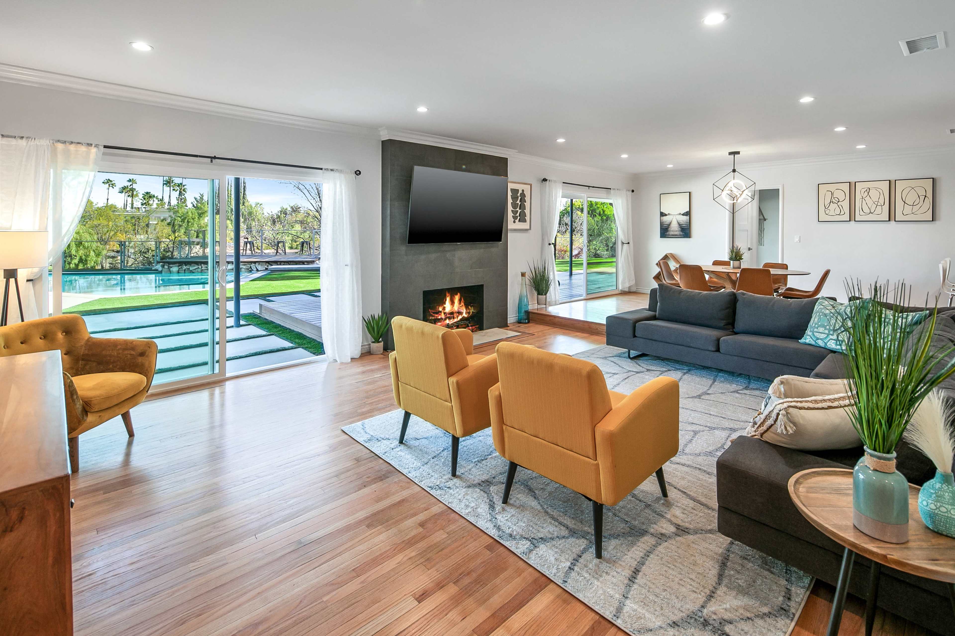 A modern living room features a fireplace, sliding glass doors opening to a pool area, and cozy seating arrangements.
