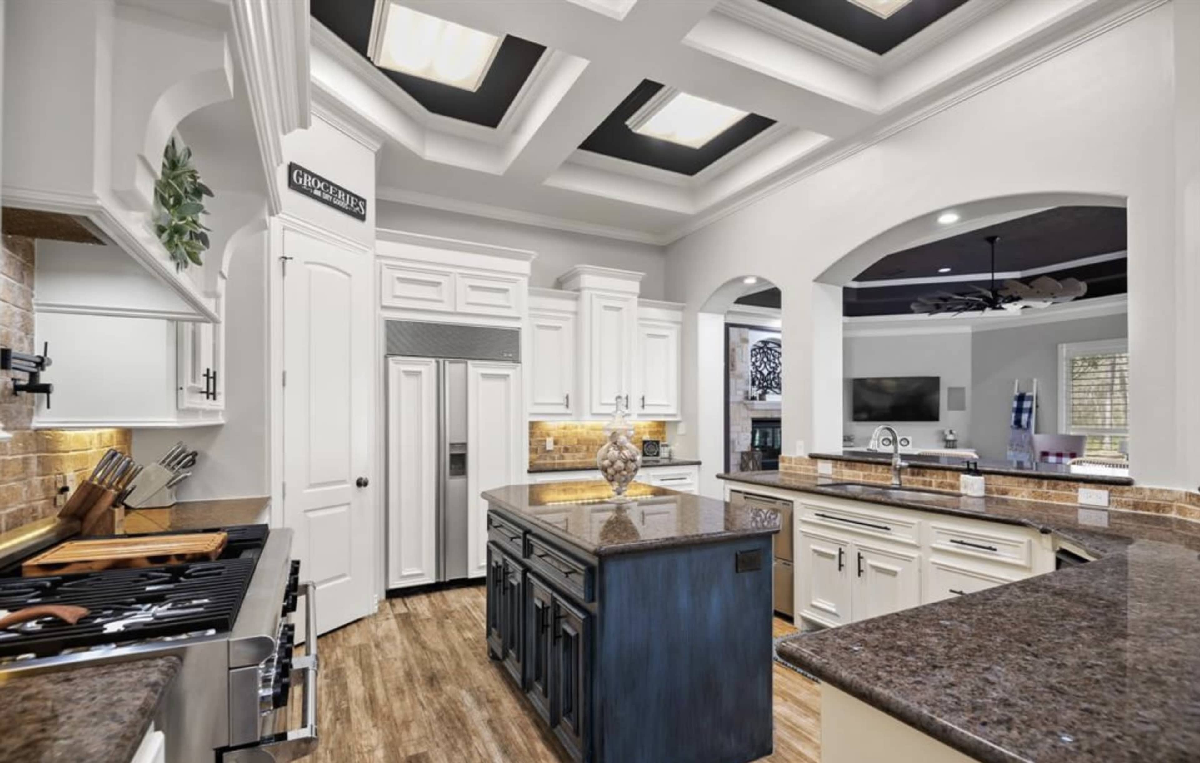 A modern kitchen with a coffered ceiling, granite countertops, white cabinetry, and stainless steel appliances.