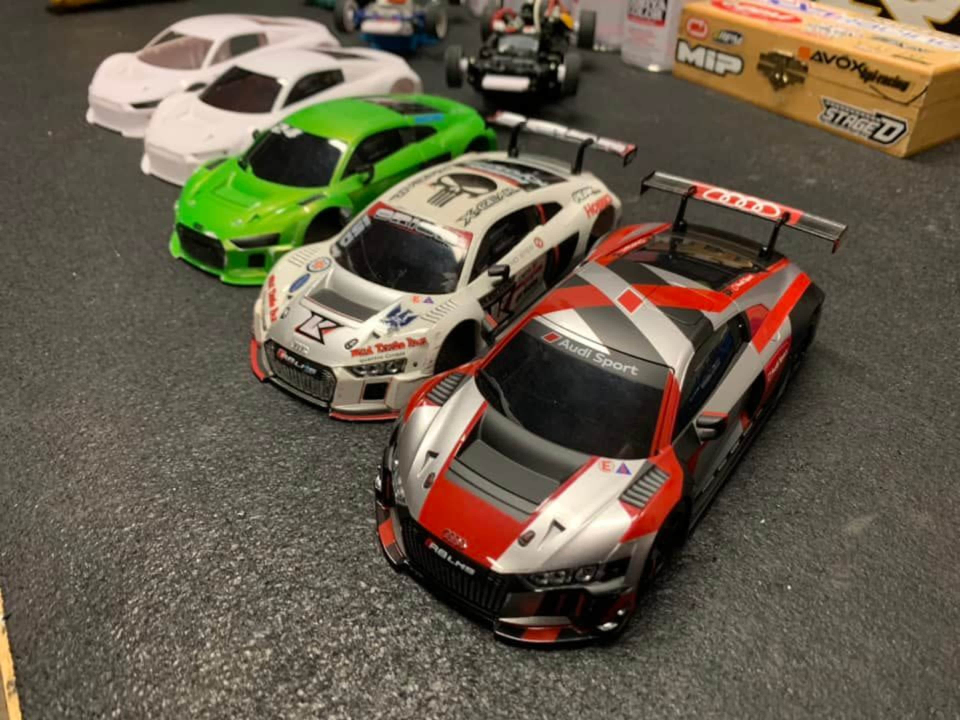 The image features a lineup of scale model racing cars in various colors, including red, green, and white, on a black surface.