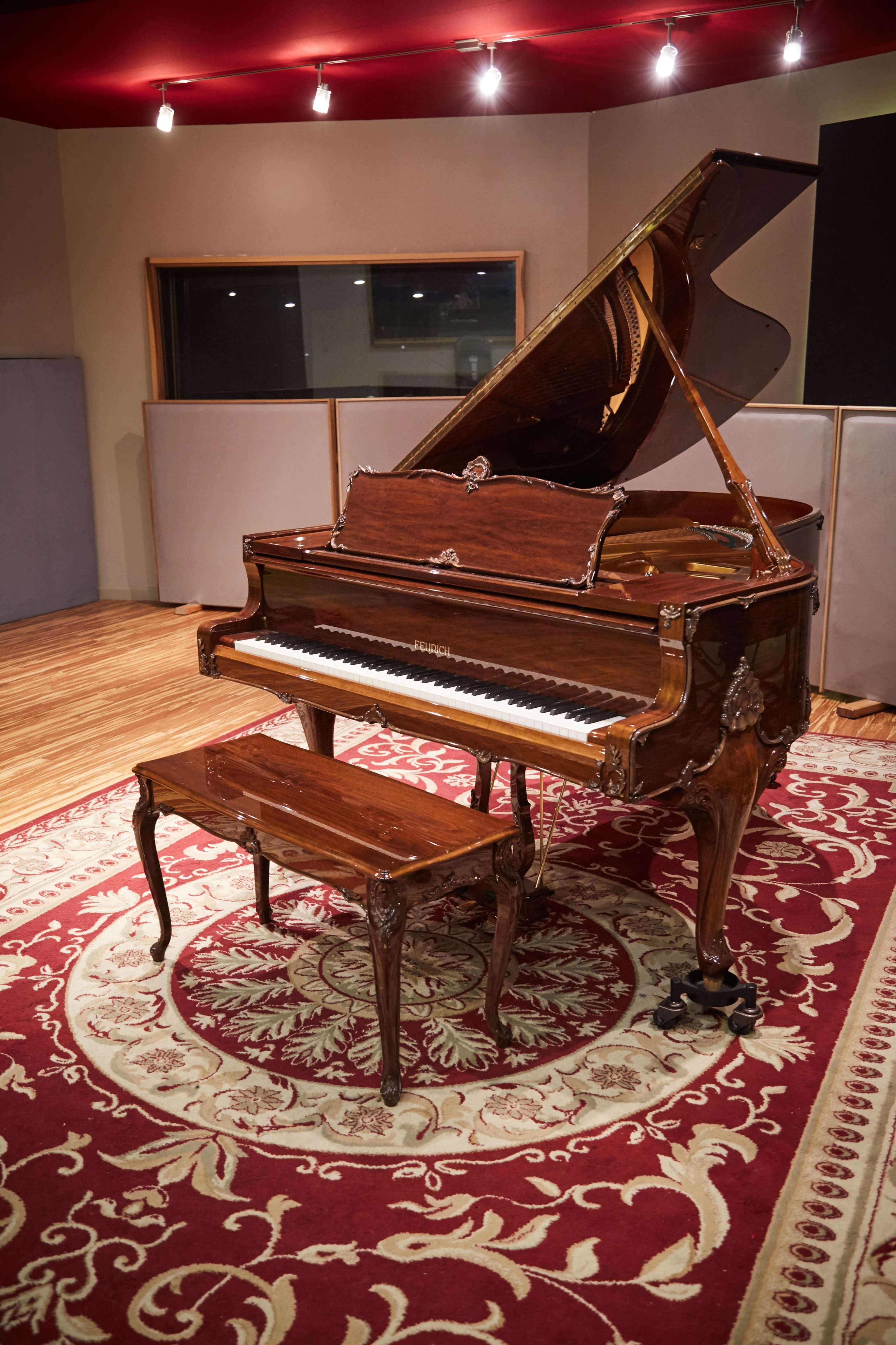 A grand piano with an ornate design sits atop a decorative rug in a recording studio.