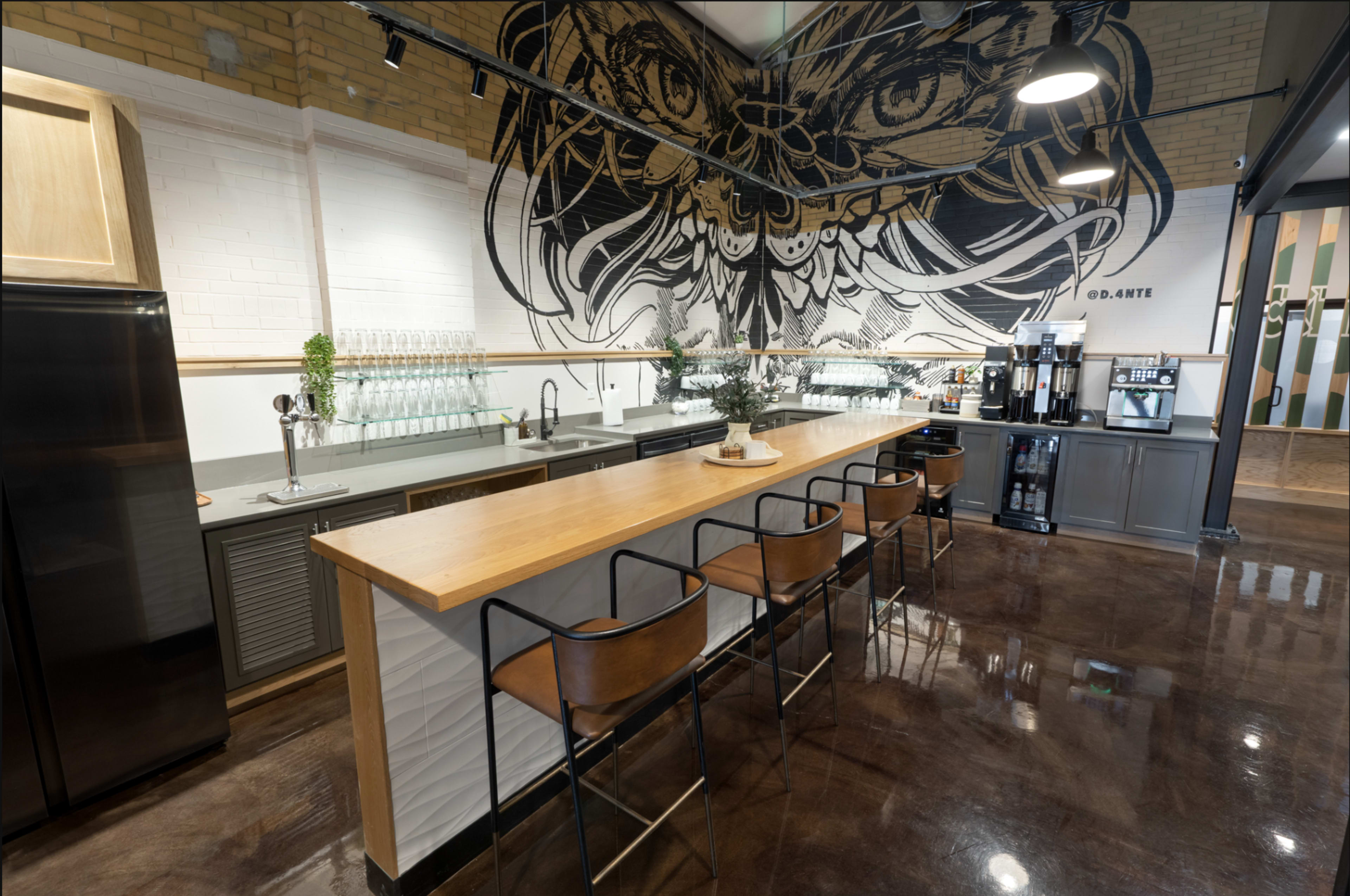 The image features a modern café interior with a long wooden counter, bar stools, and a large mural of an owl on the wall.