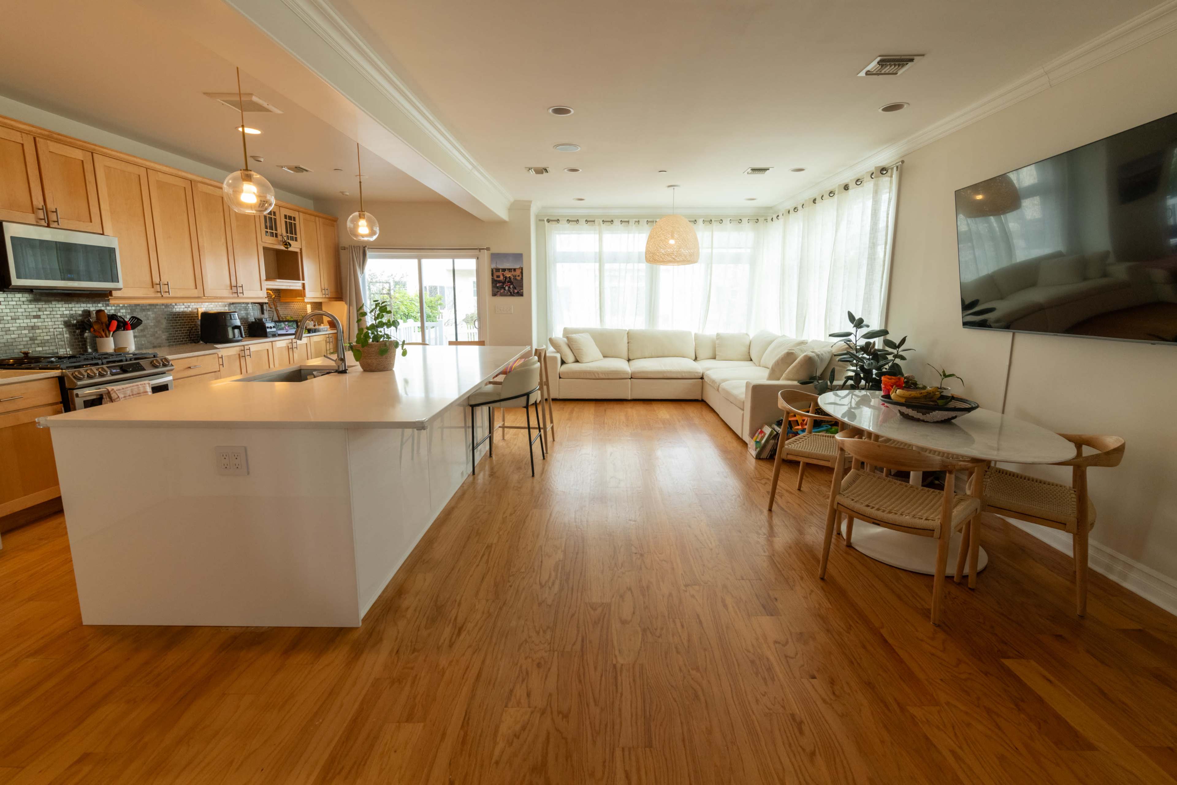 The image shows a modern open-concept living area with a large sectional sofa, a dining table, and a kitchen visible in the background.