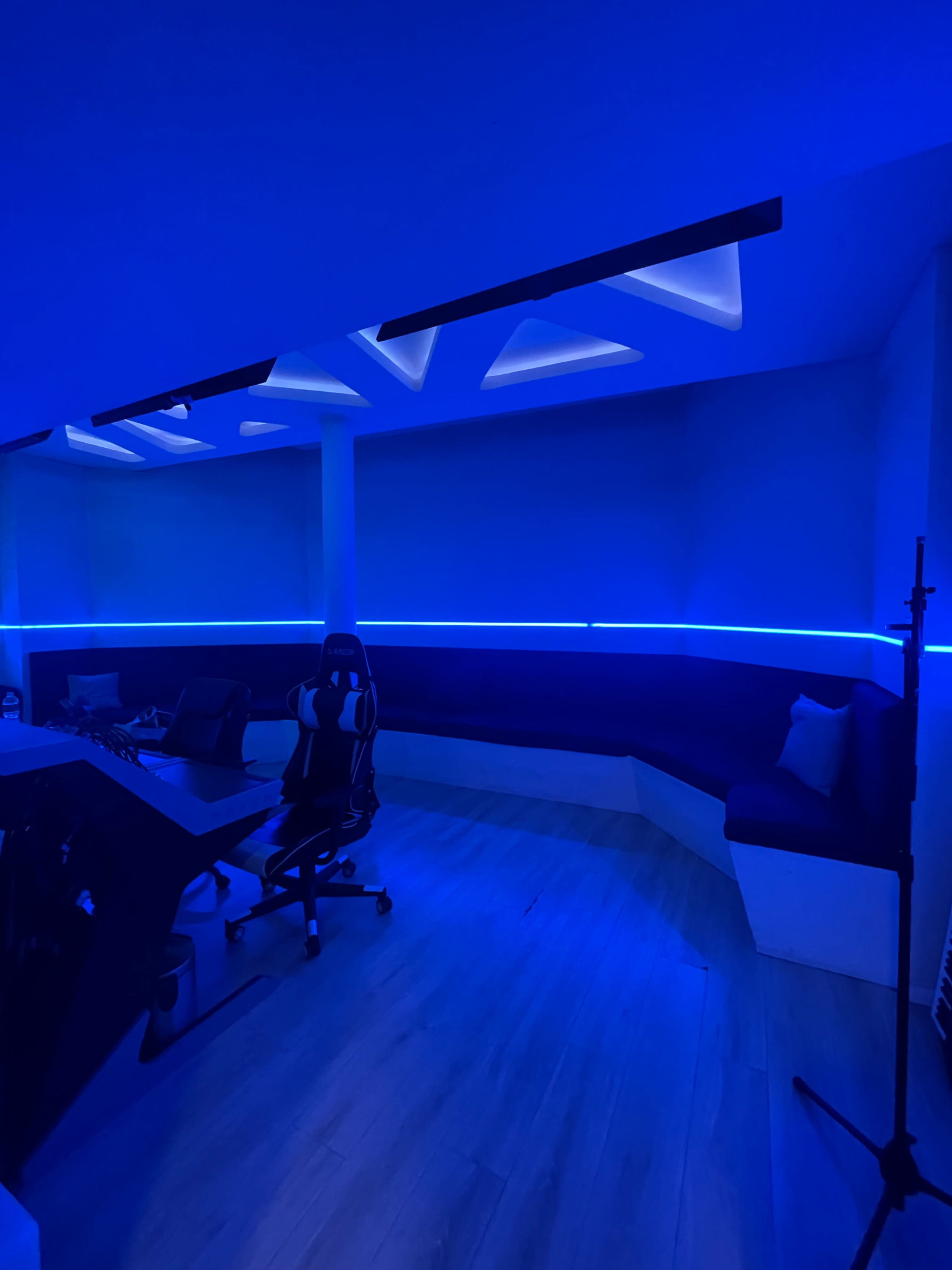 A modern room features blue LED lighting, a dark seating area, and ergonomic chairs around a desk.