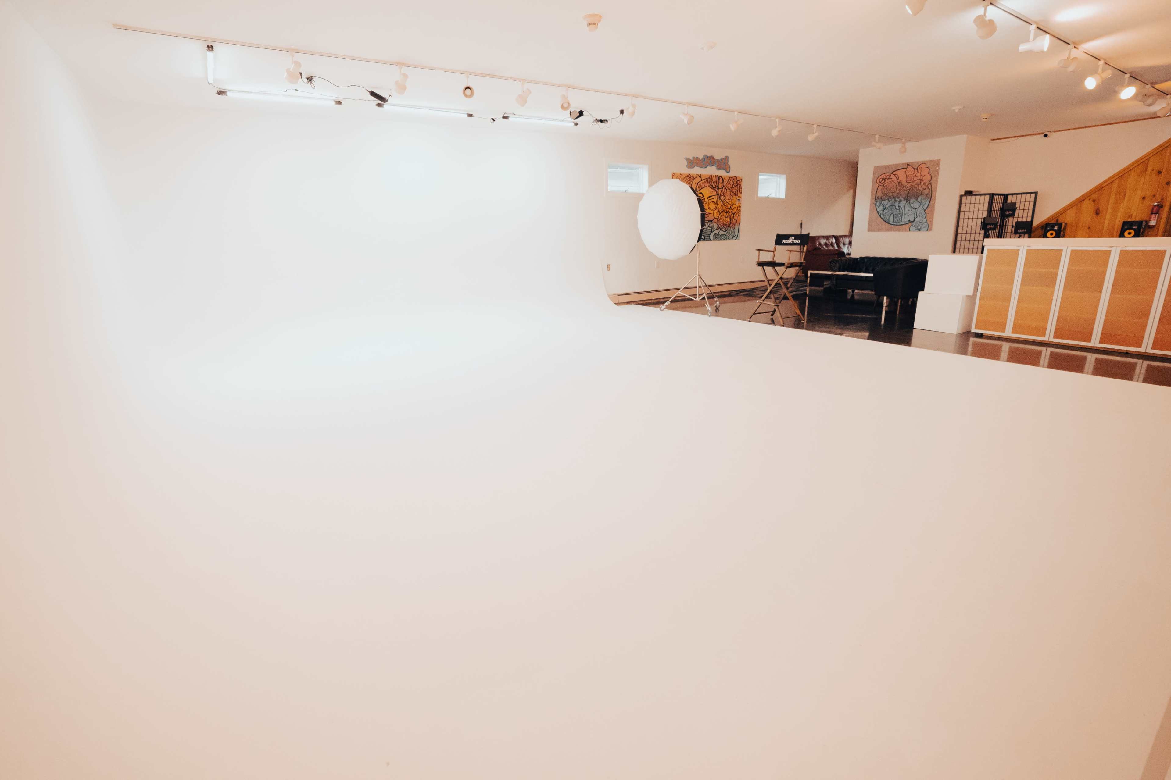 A spacious studio with a seamless white backdrop, soft lighting, and a few artistic decorations on the walls.