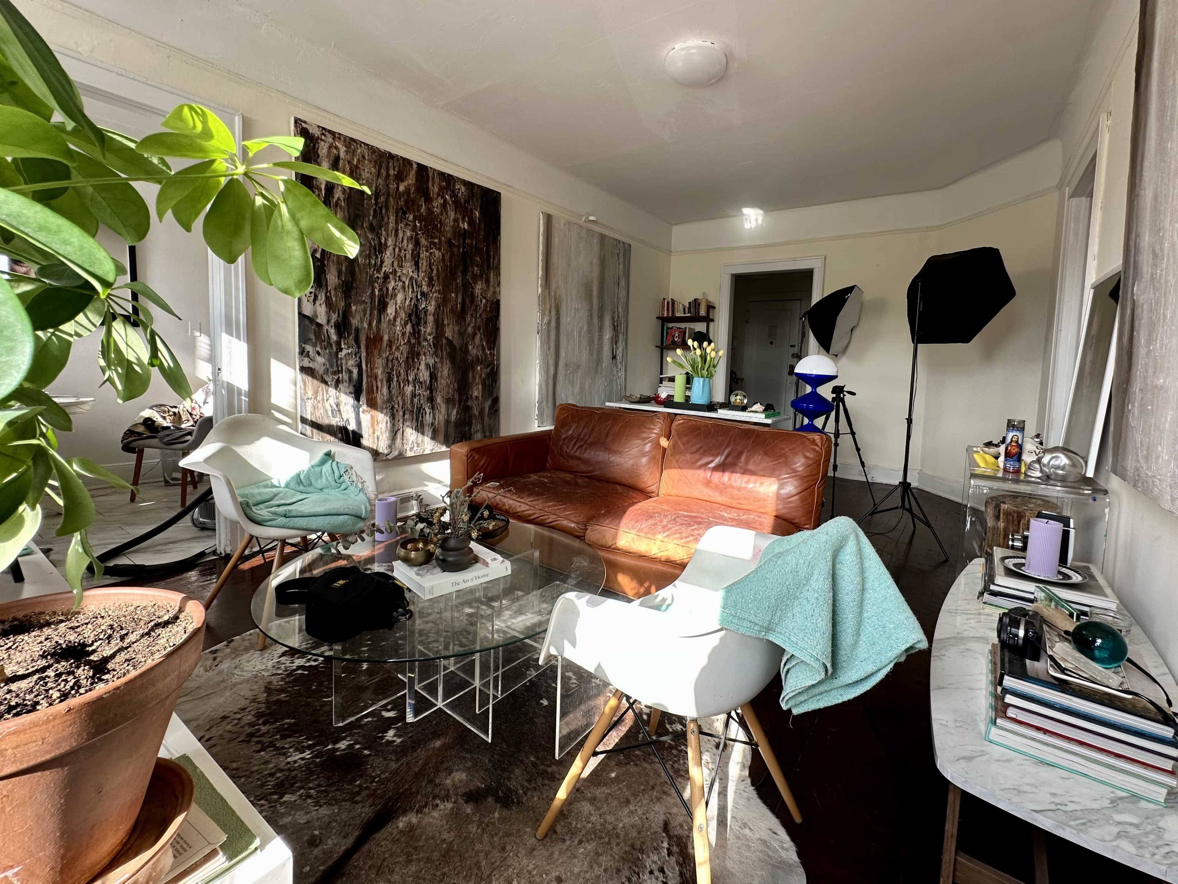 The image shows a living room with a brown leather sofa, a glass coffee table, modern chairs, and various decor items arranged on a side table and shelves.