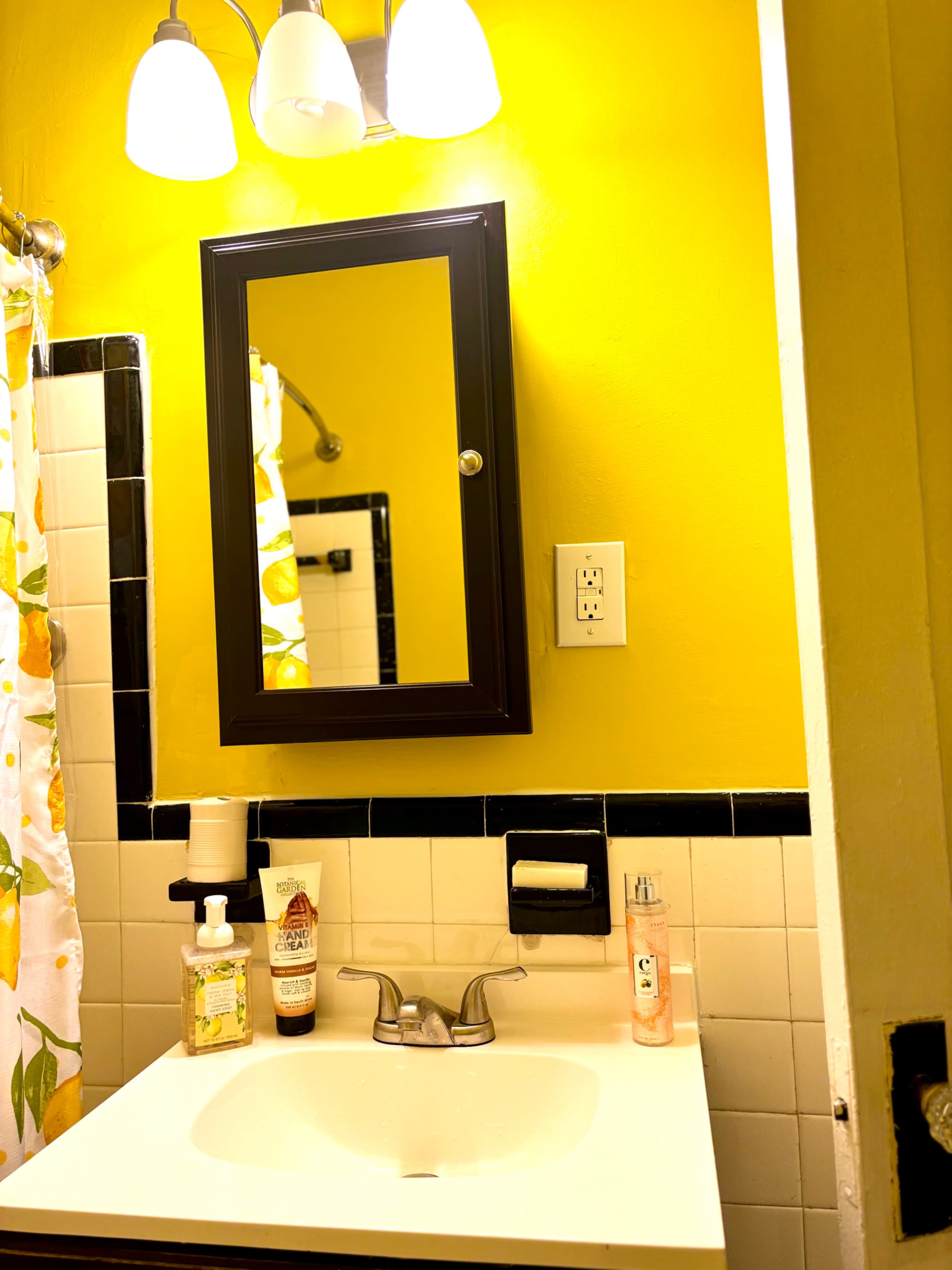 The image shows a bathroom sink area with a yellow wall, a mirror above the sink, and various toiletries on the countertop.