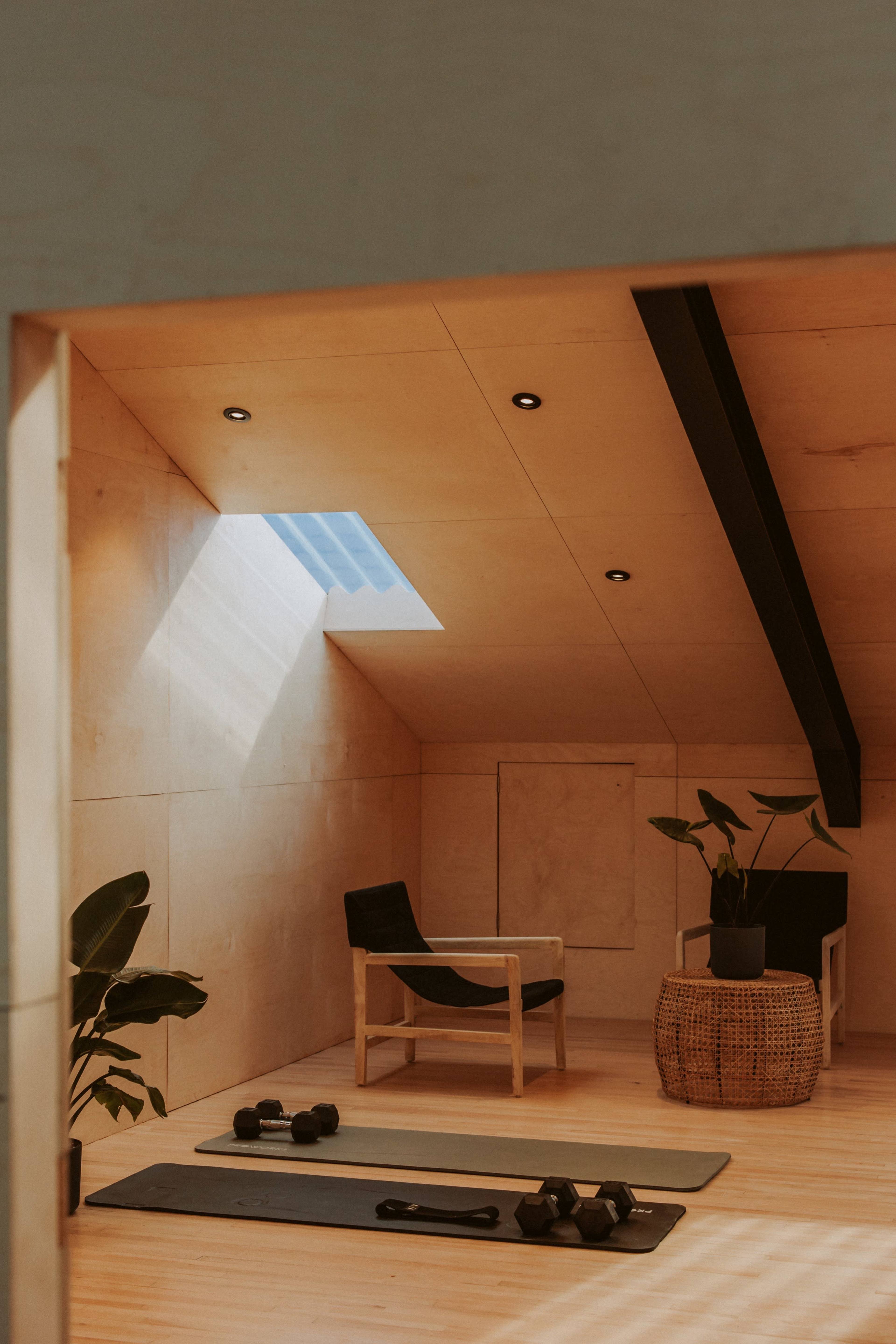 A minimalist workout space featuring exercise mats, weights, and a small seating area with natural light streaming through a skylight.