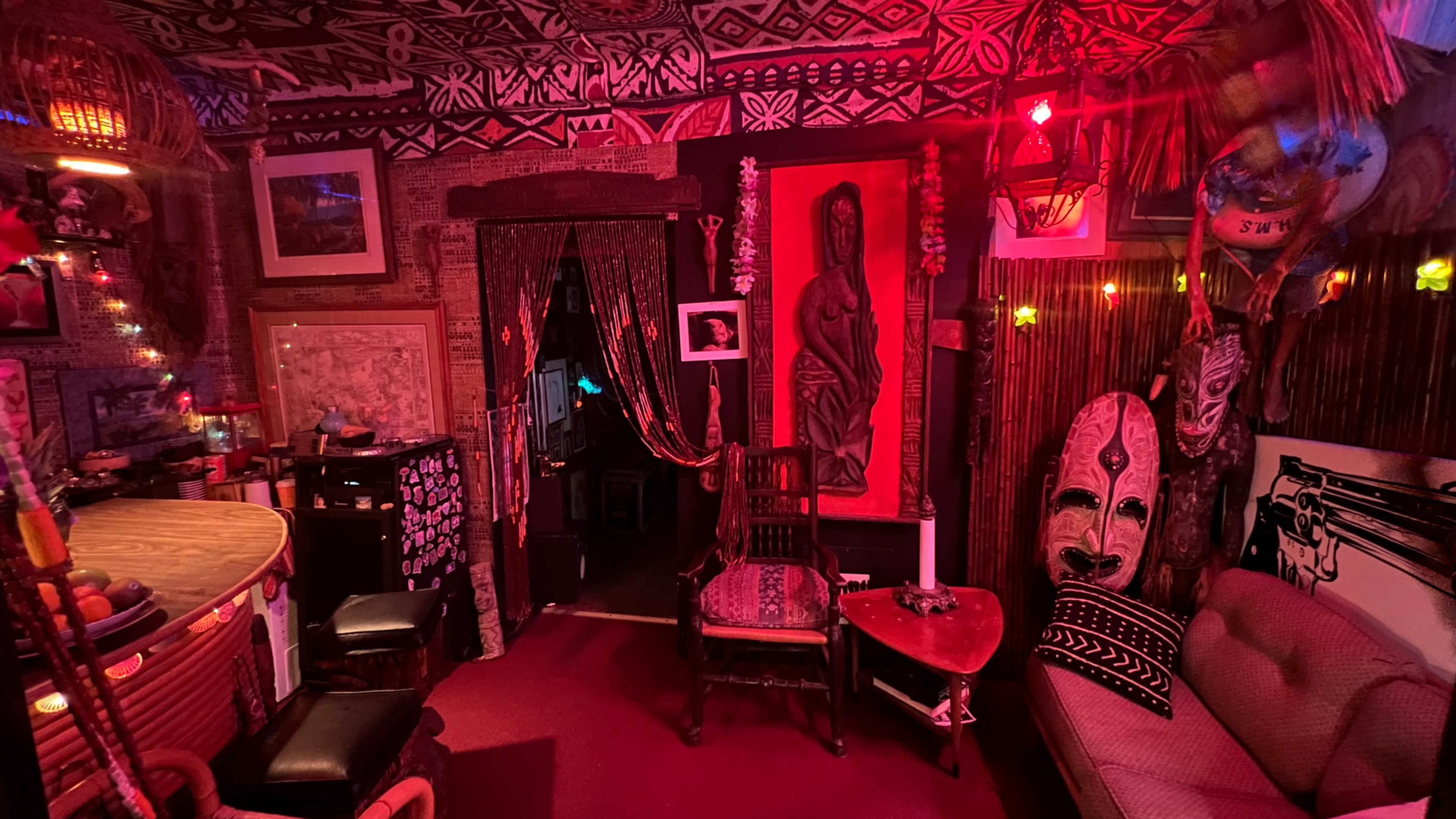 The scene depicts a warmly lit room adorned with tribal patterns, featuring a mix of decorative art pieces, including a large statue and a mask, along with a cozy seating area.