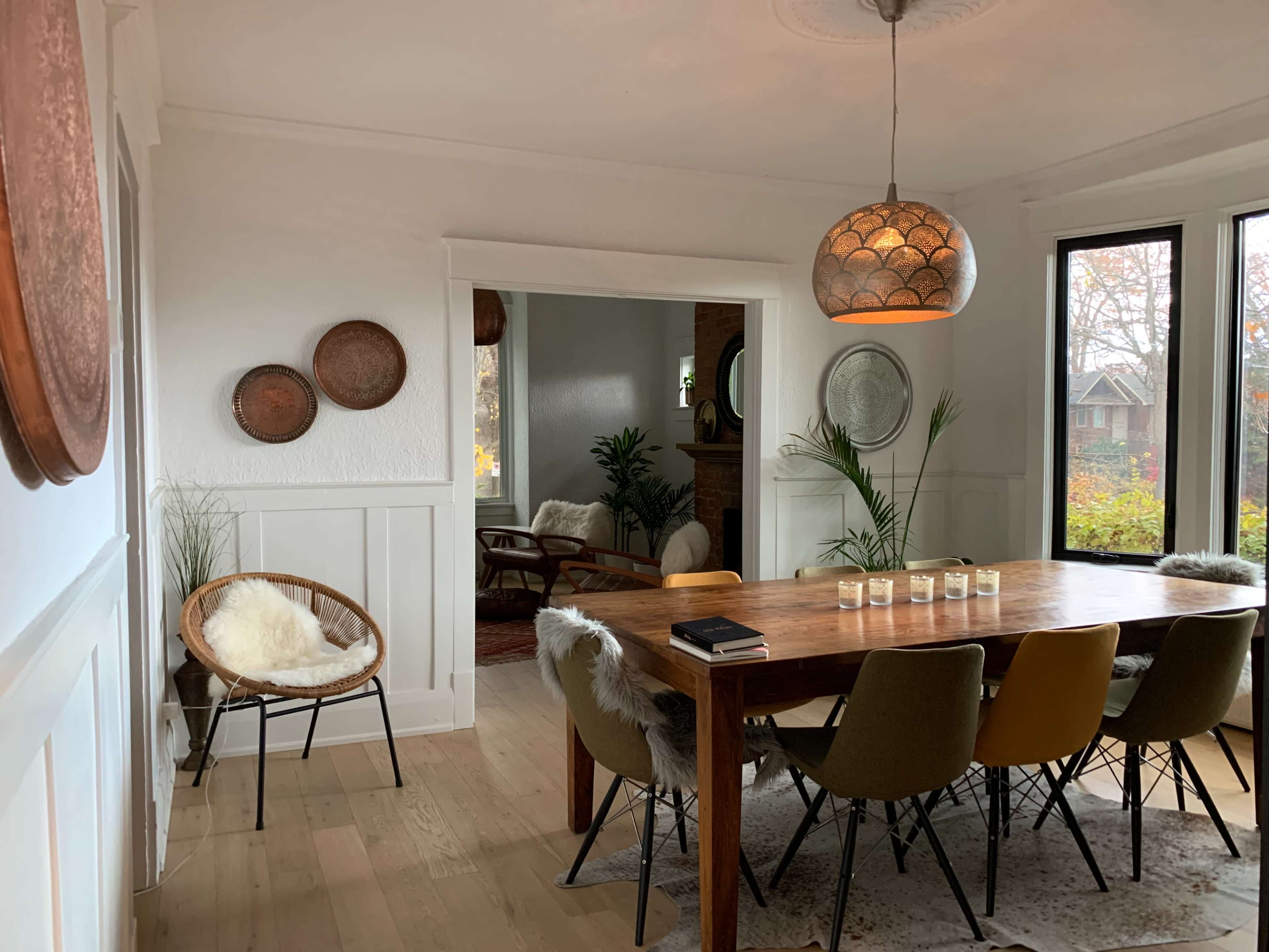 A dining room features a wooden table surrounded by eight chairs, with a pendant light above and decorative plates on the walls.