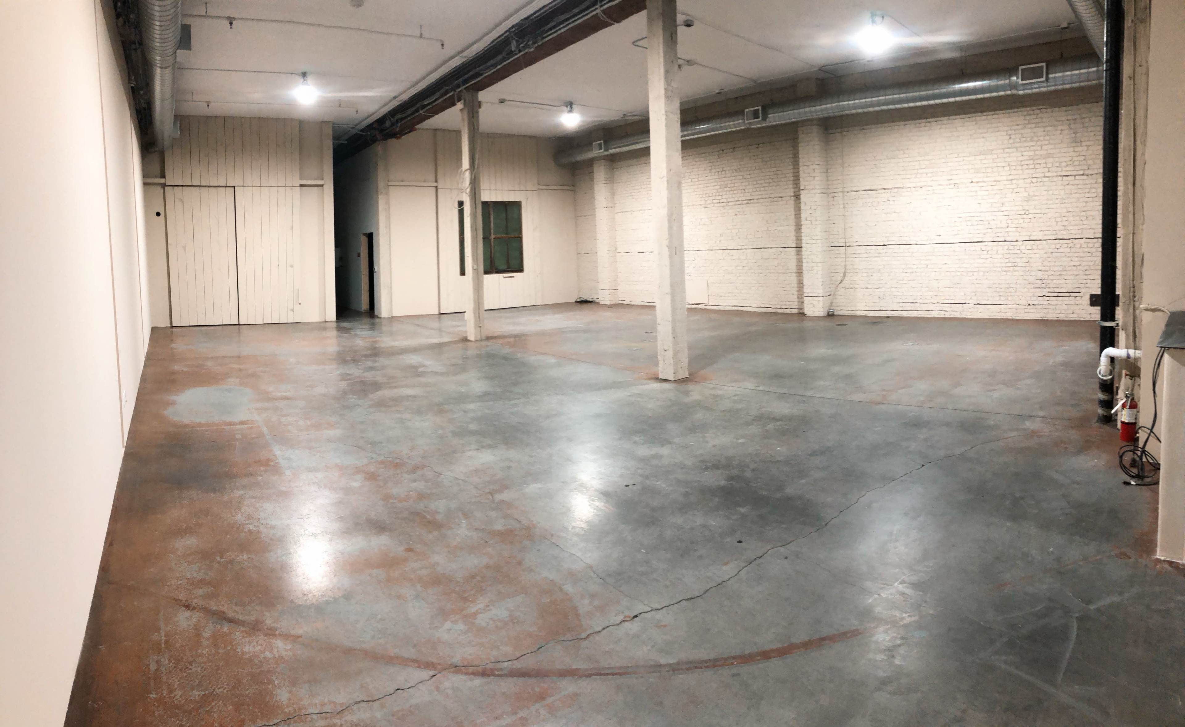 An empty industrial space with concrete flooring, exposed brick walls, and concrete columns.