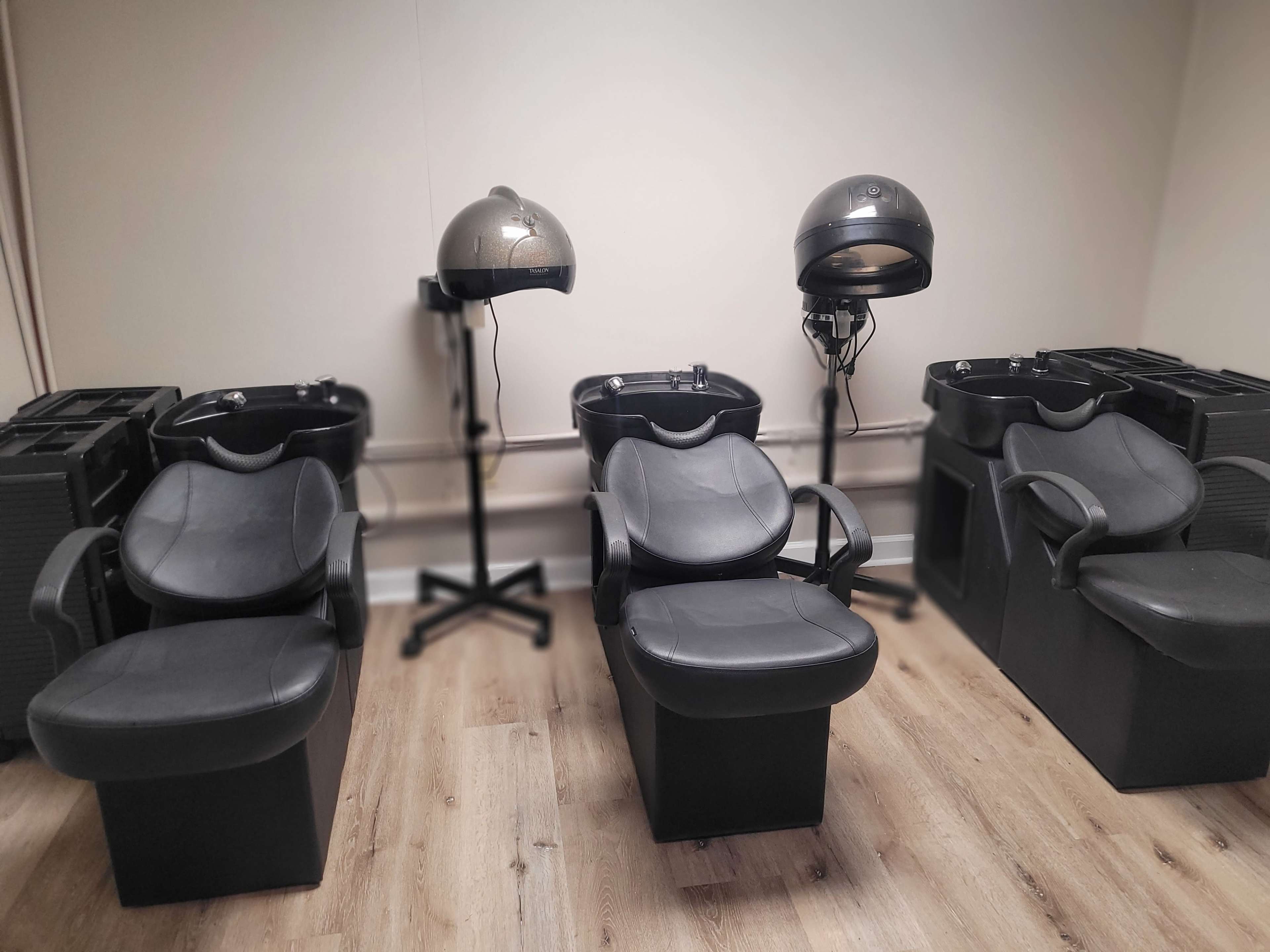 The image shows a hair salon interior featuring three black styling chairs and two hooded hair dryers.