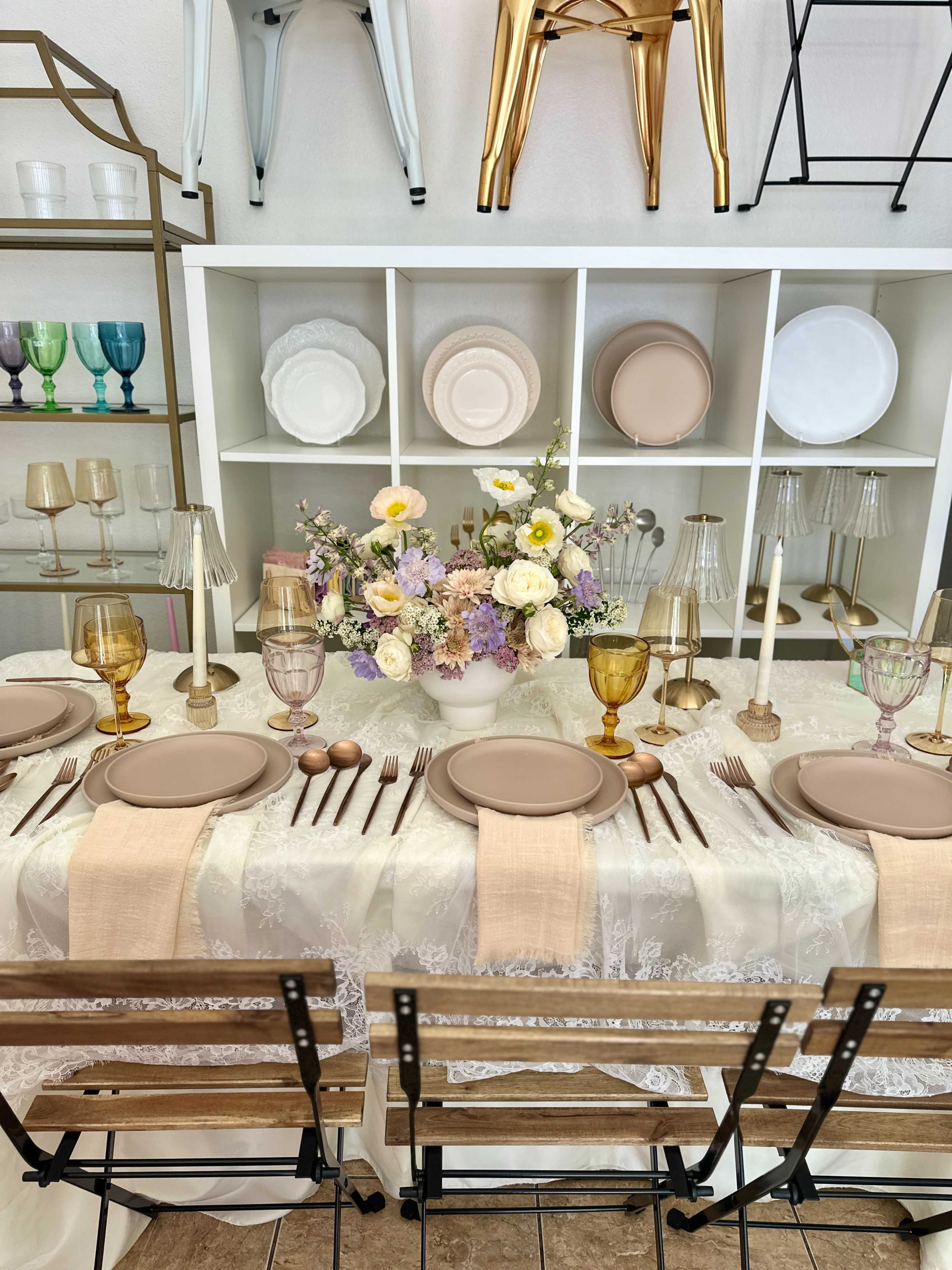 A dining table is set with elegant plates, glasses, and utensils, arranged under a display of various dishware and decorative items.