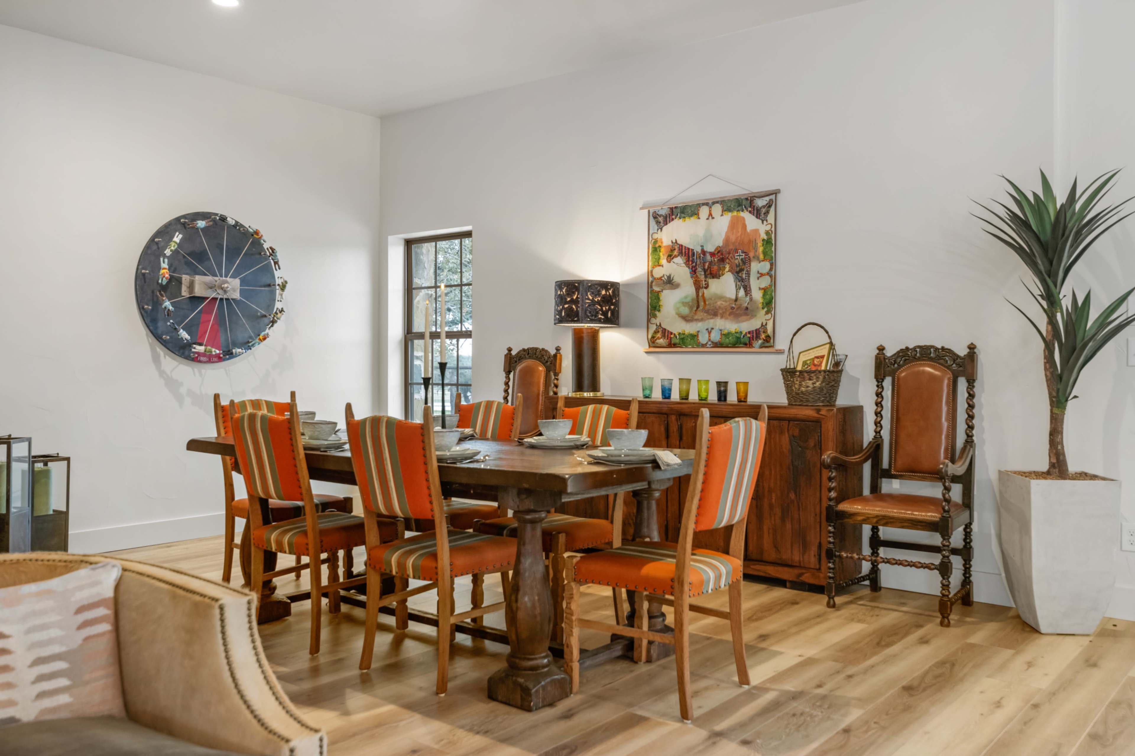 The image shows a dining area with a large wooden table surrounded by eight striped chairs, a side cabinet, and decorative wall art.