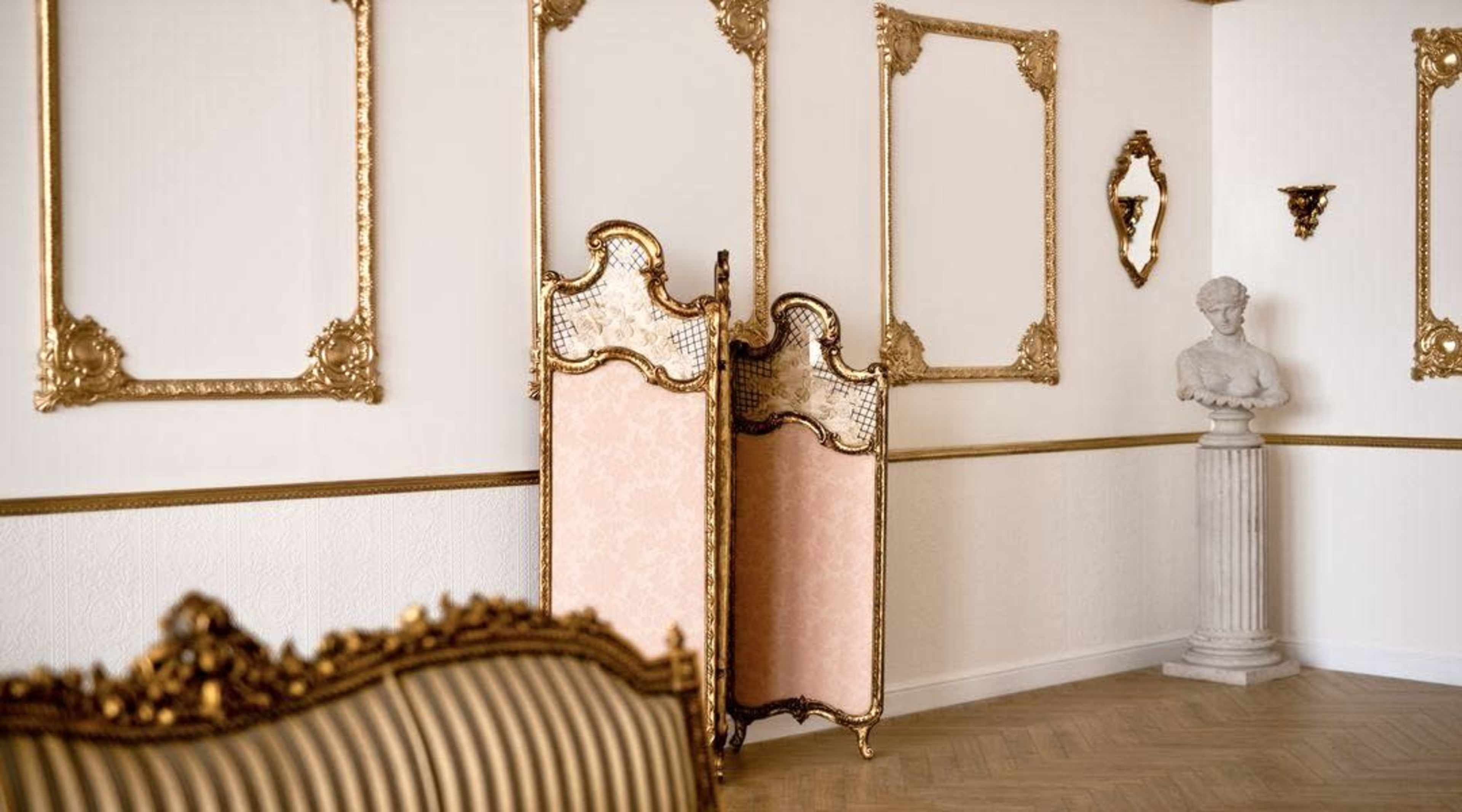 The scene features a room with ornate gold-trimmed mirrors, a decorative room divider, and a classical bust on a pedestal against light-colored walls.