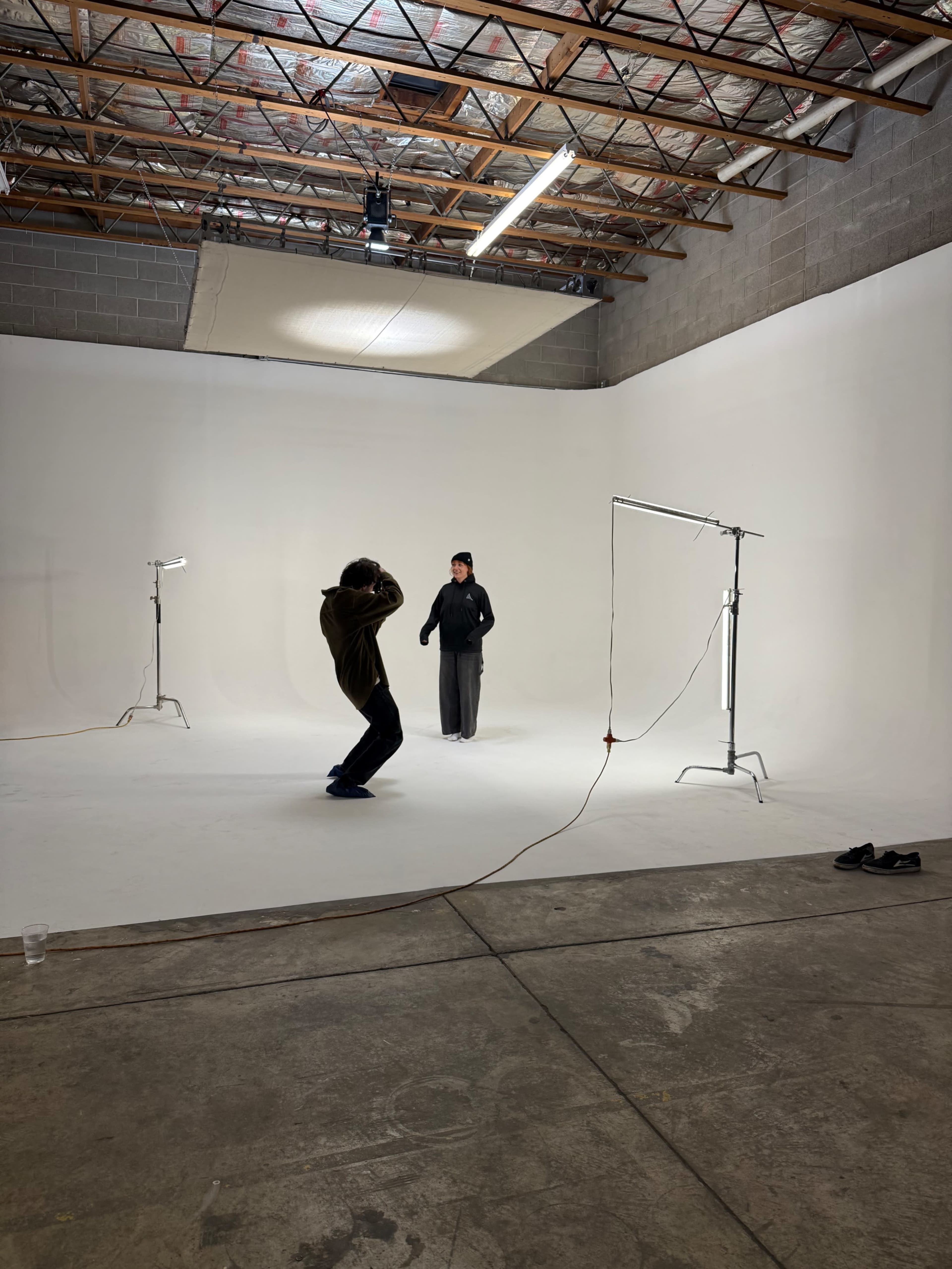 A photographer is capturing images of a model in a spacious, well-lit studio with a white backdrop.