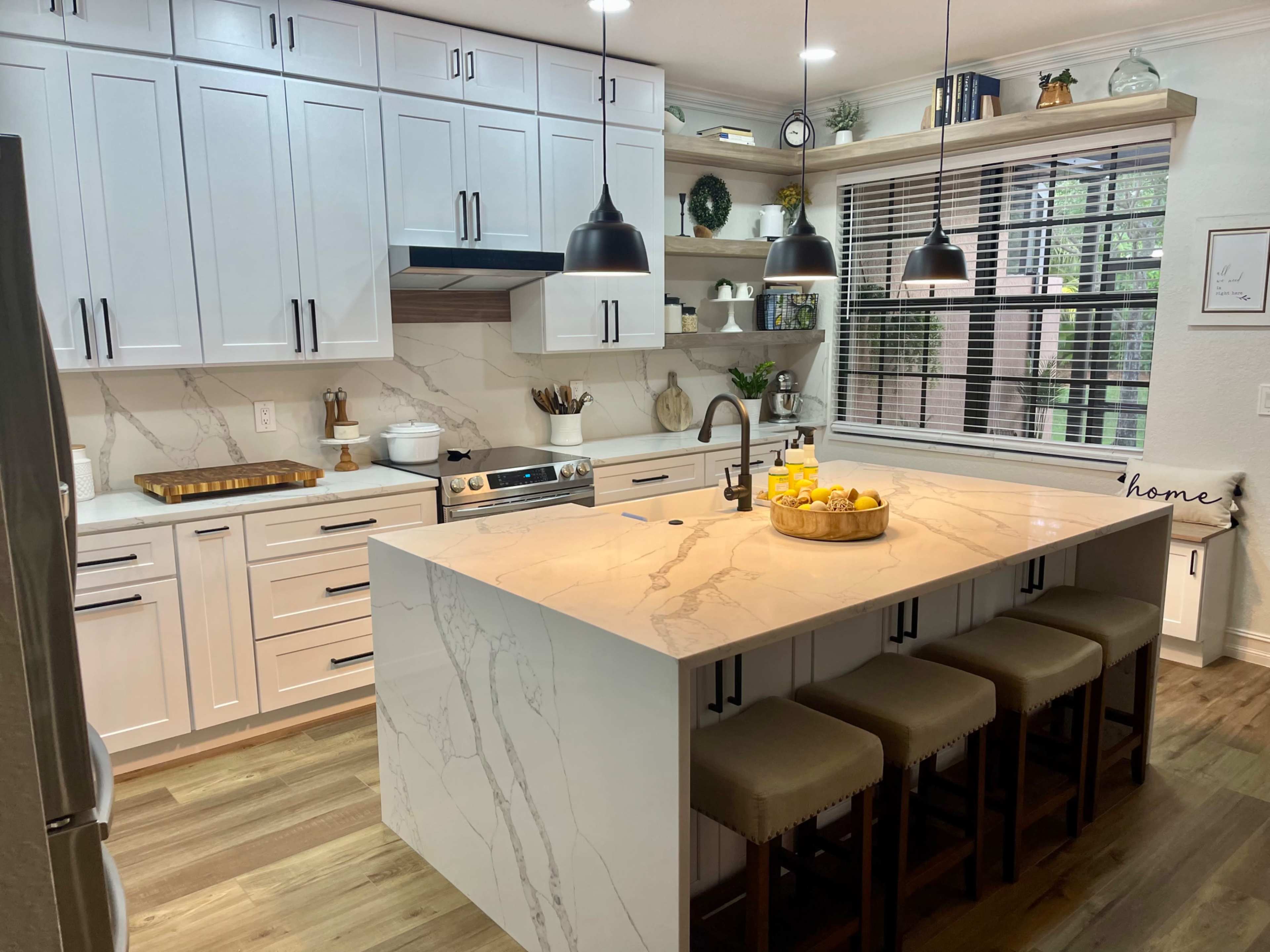 A modern kitchen with white cabinetry, a large marble island featuring barstool seating, and pendant lights illuminating the space.