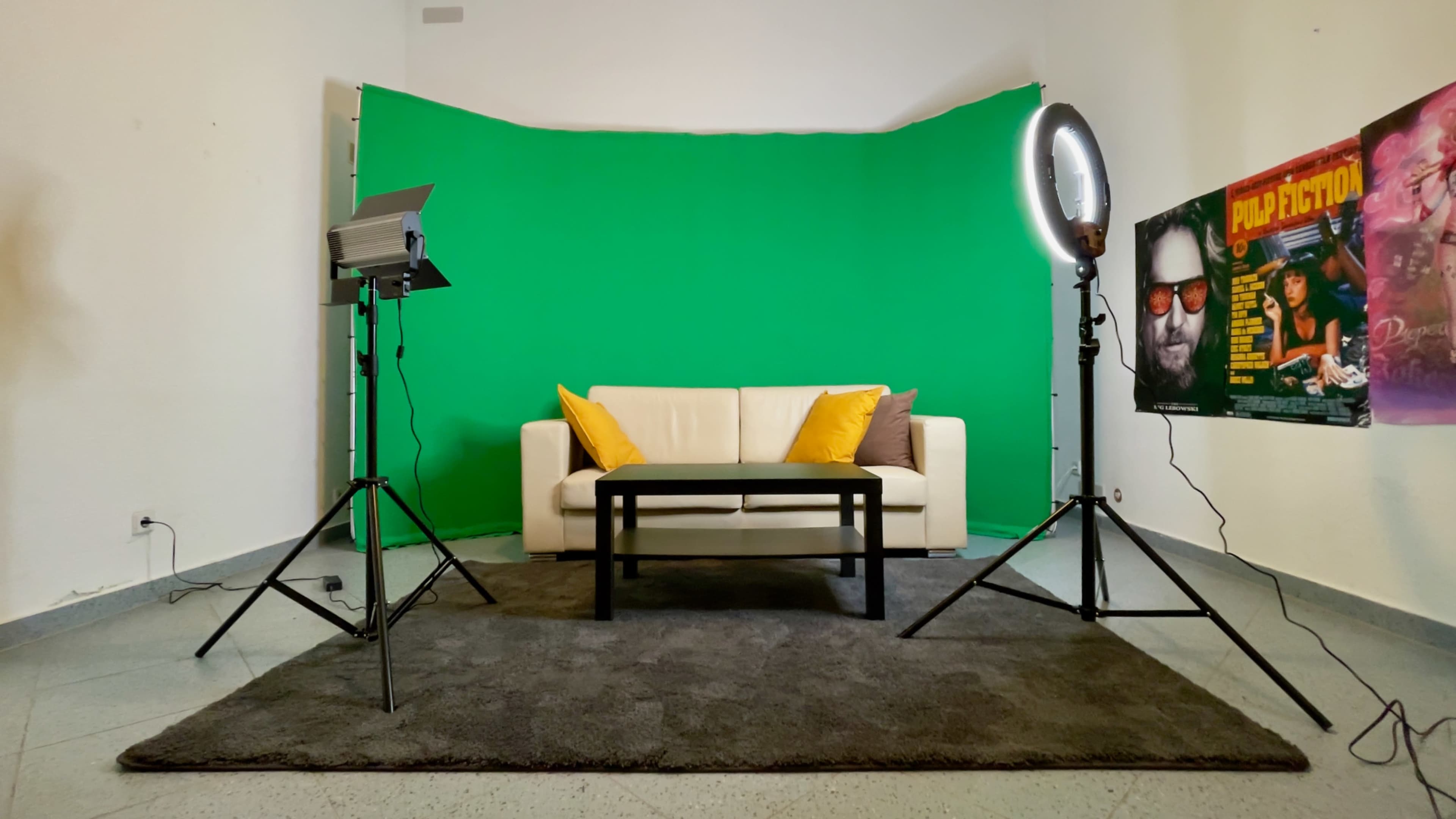 The scene features a white couch with yellow pillows in front of a green backdrop, flanked by a light source on a stand and a poster on a stand.