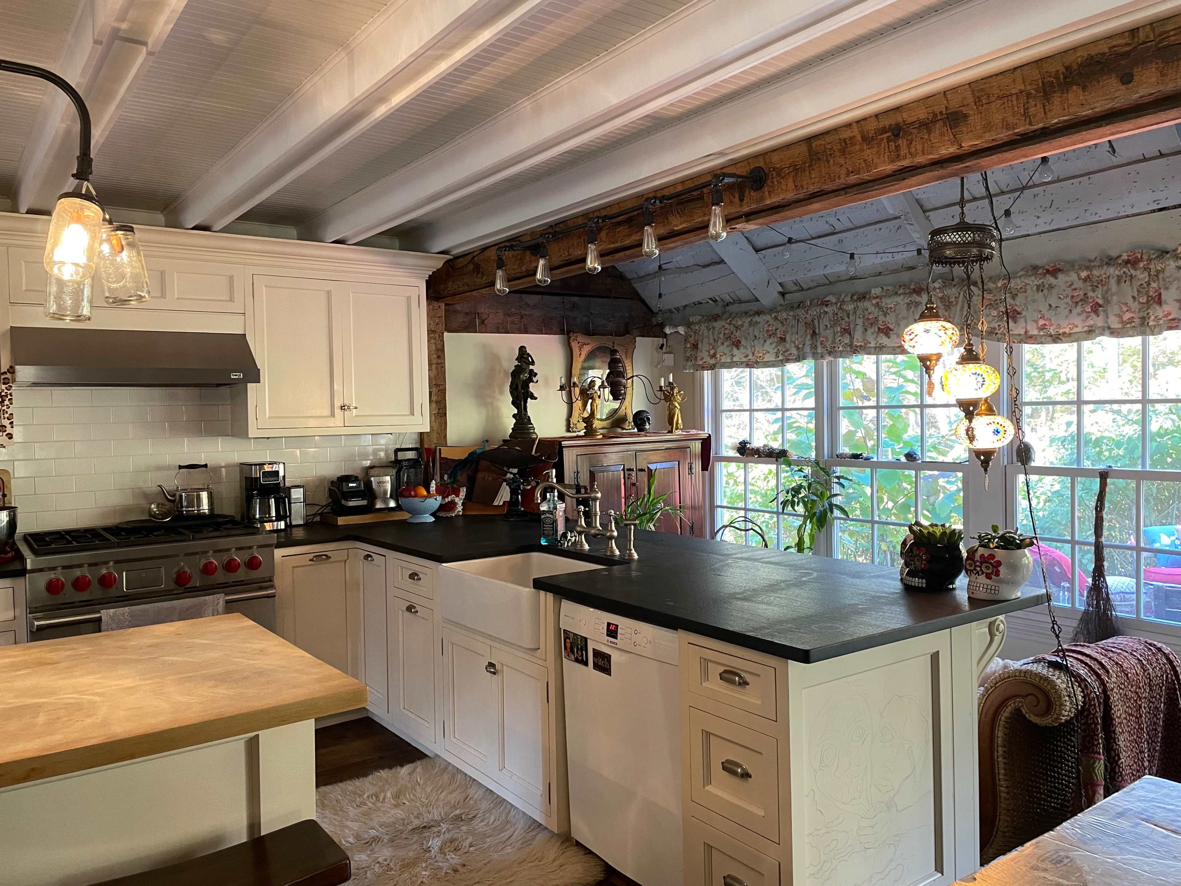 A modern kitchen with white cabinets, a large stove, and a countertop, featuring natural light from a window adorned with floral curtains.
