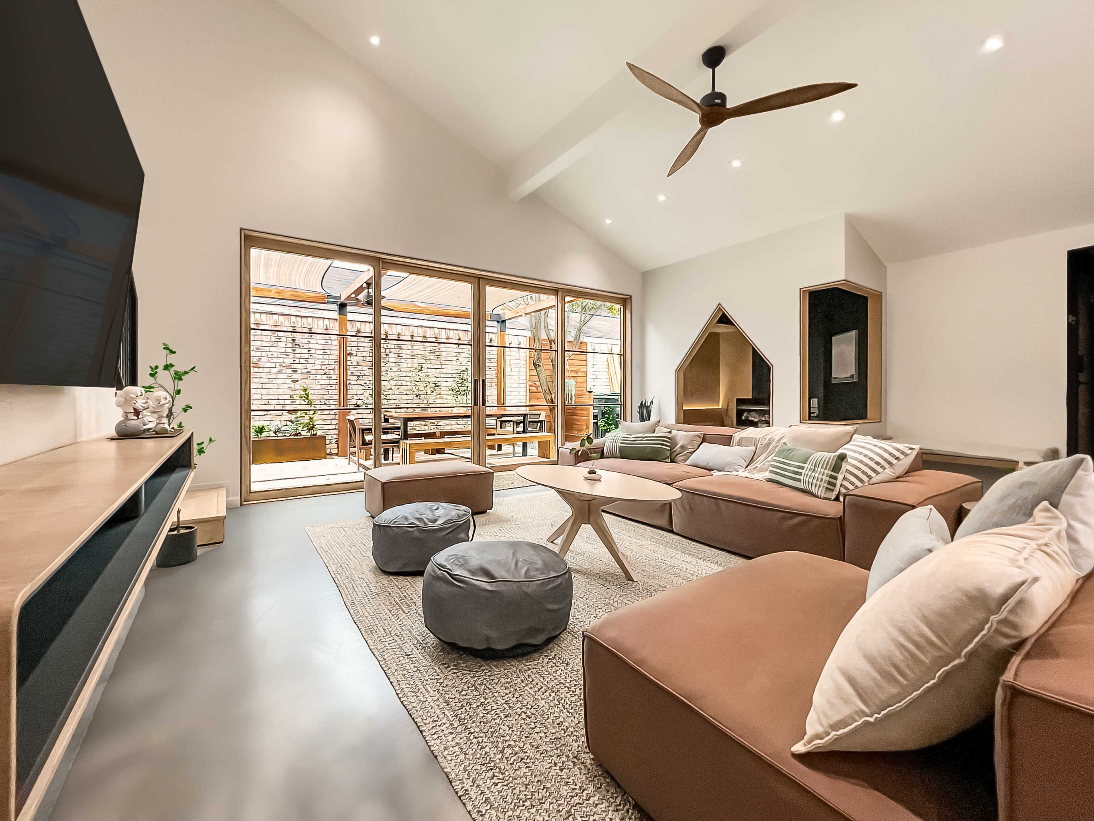 A modern living room with a large sectional sofa, a coffee table, and glass doors leading to an outdoor seating area.