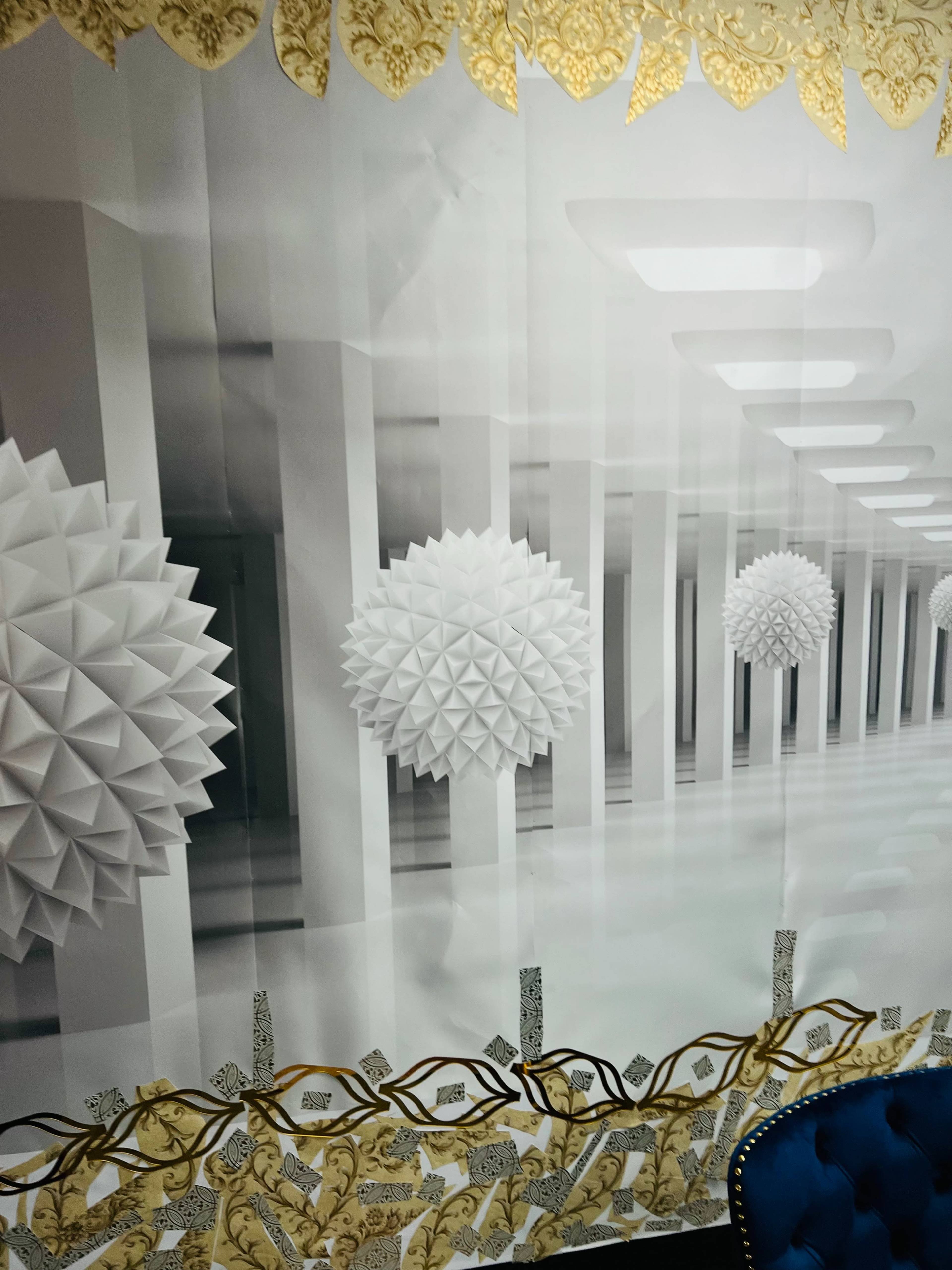 A large wall mural features a black-and-white hallway with three-dimensional geometric shapes hanging from the ceiling, bordered by an ornate gold and white design.