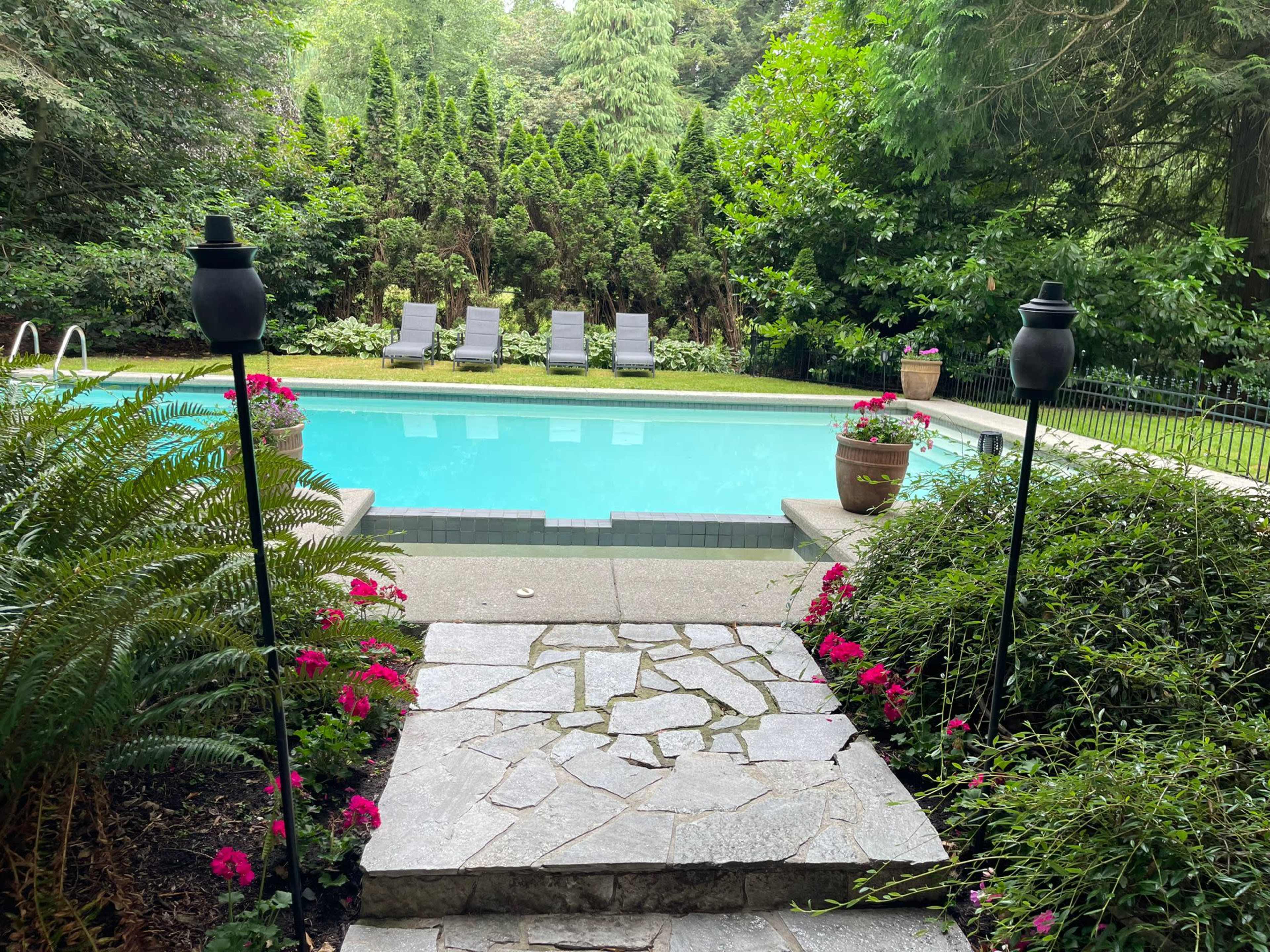 A stone pathway leads to a swimming pool surrounded by greenery and lounge chairs.