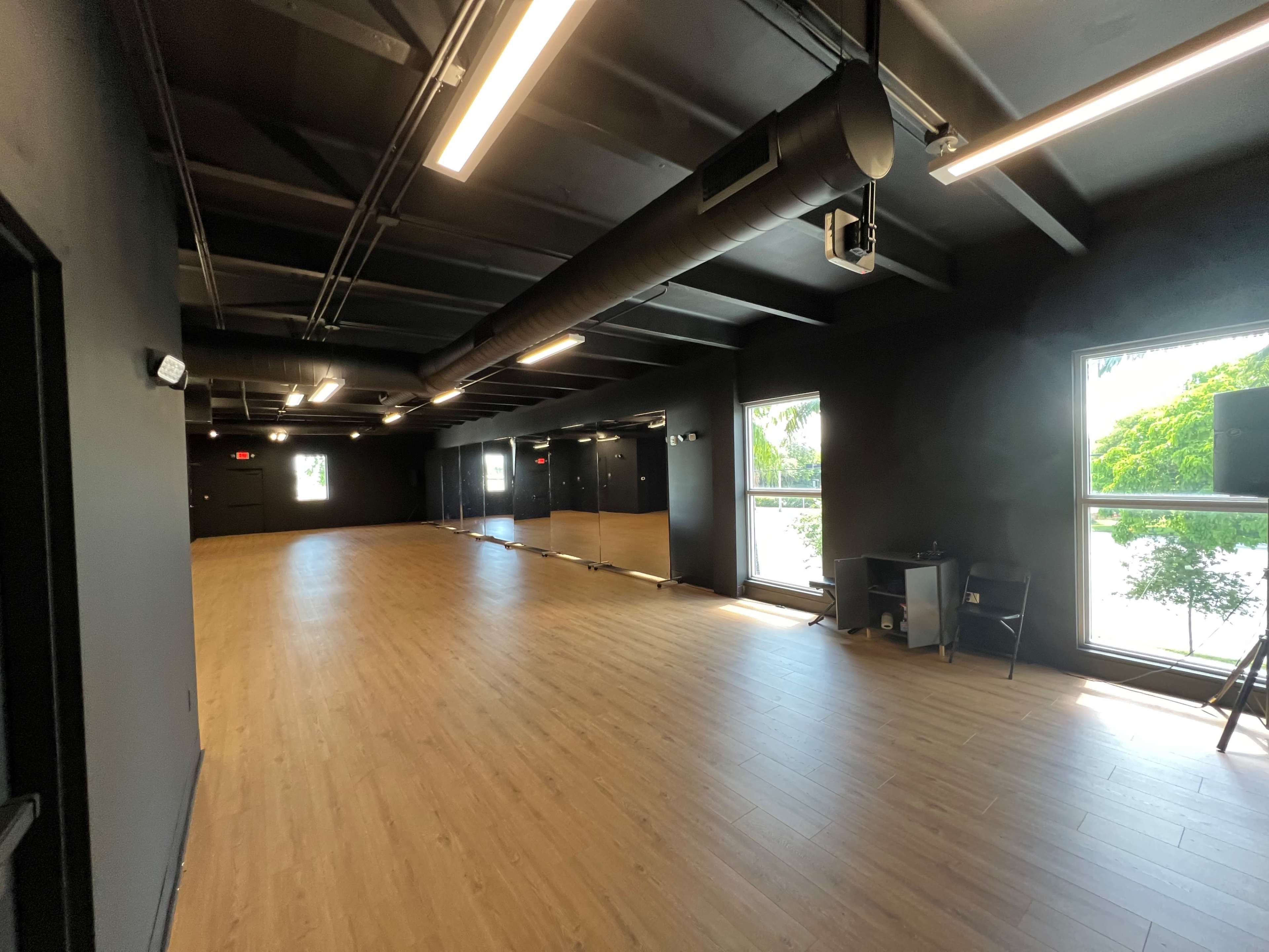 An empty studio space with black walls, wooden flooring, and large windows on one side.