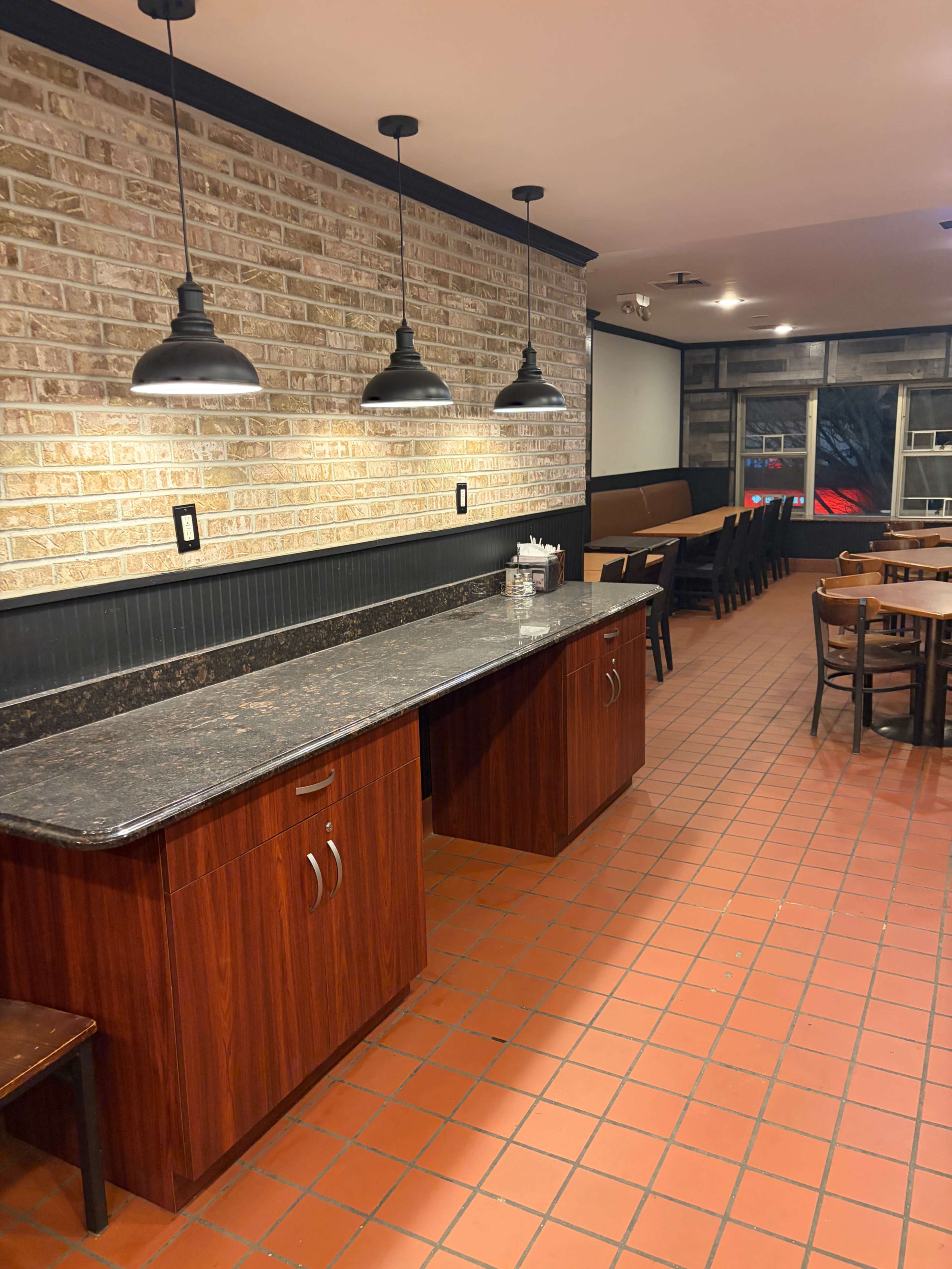 The image shows a restaurant interior with a wooden countertop, black pendant lights, and tiled flooring.