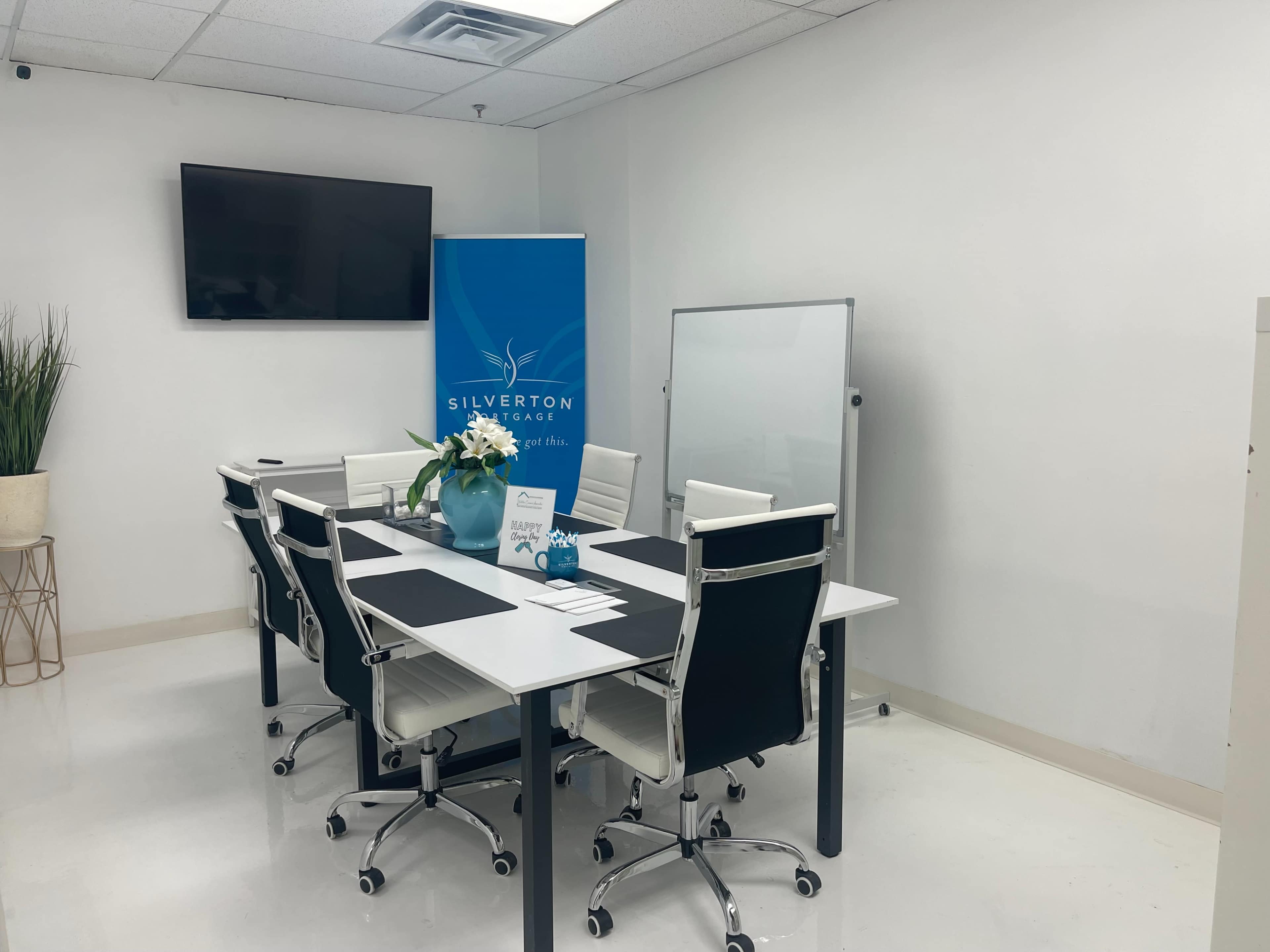 A modern conference room is set up with a large table, white chairs, a flat-screen TV, a whiteboard, and a display banner for Silverton Financial.
