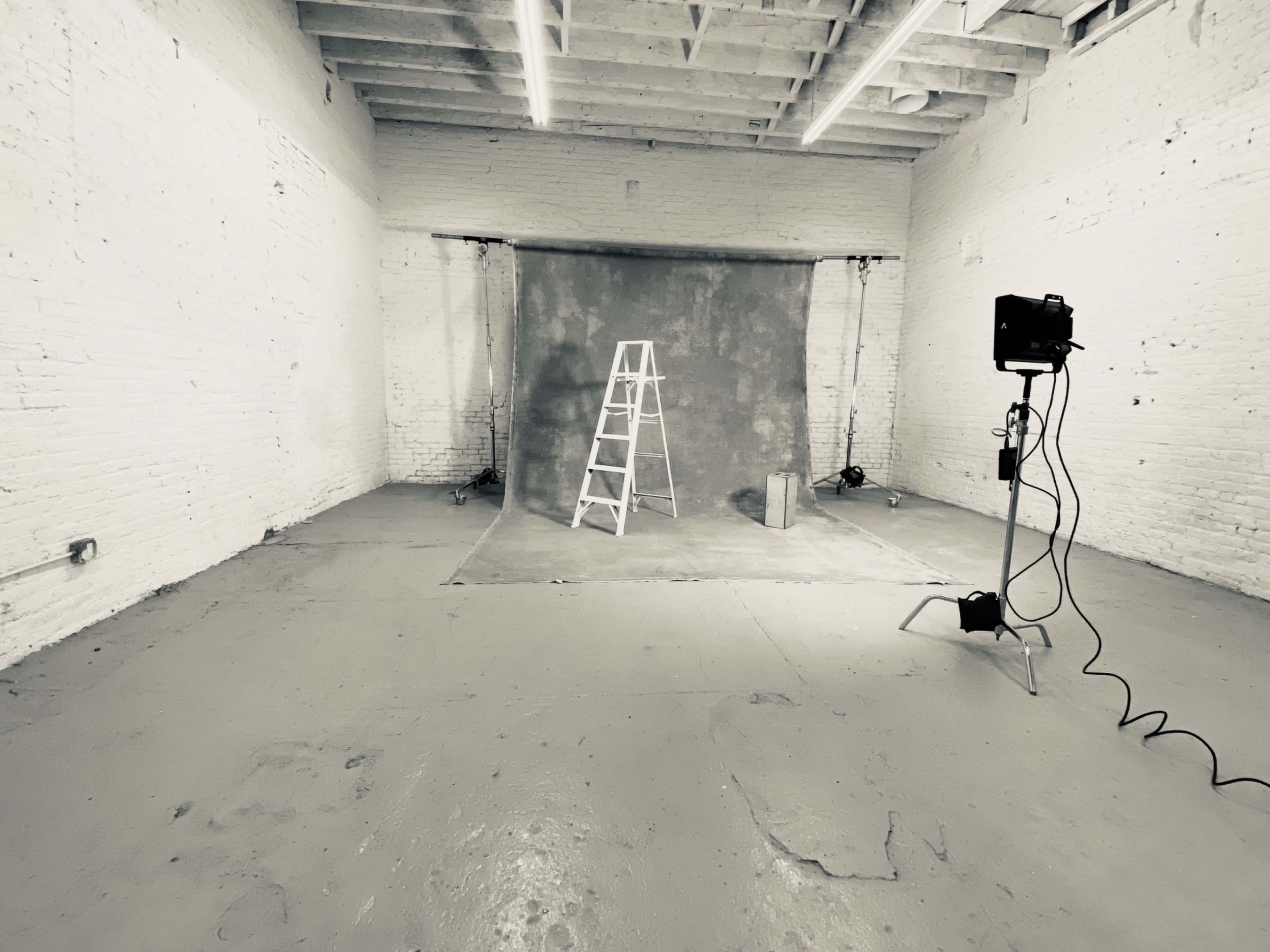 The image shows an empty photography studio with a ladder, backdrop, and light setup.