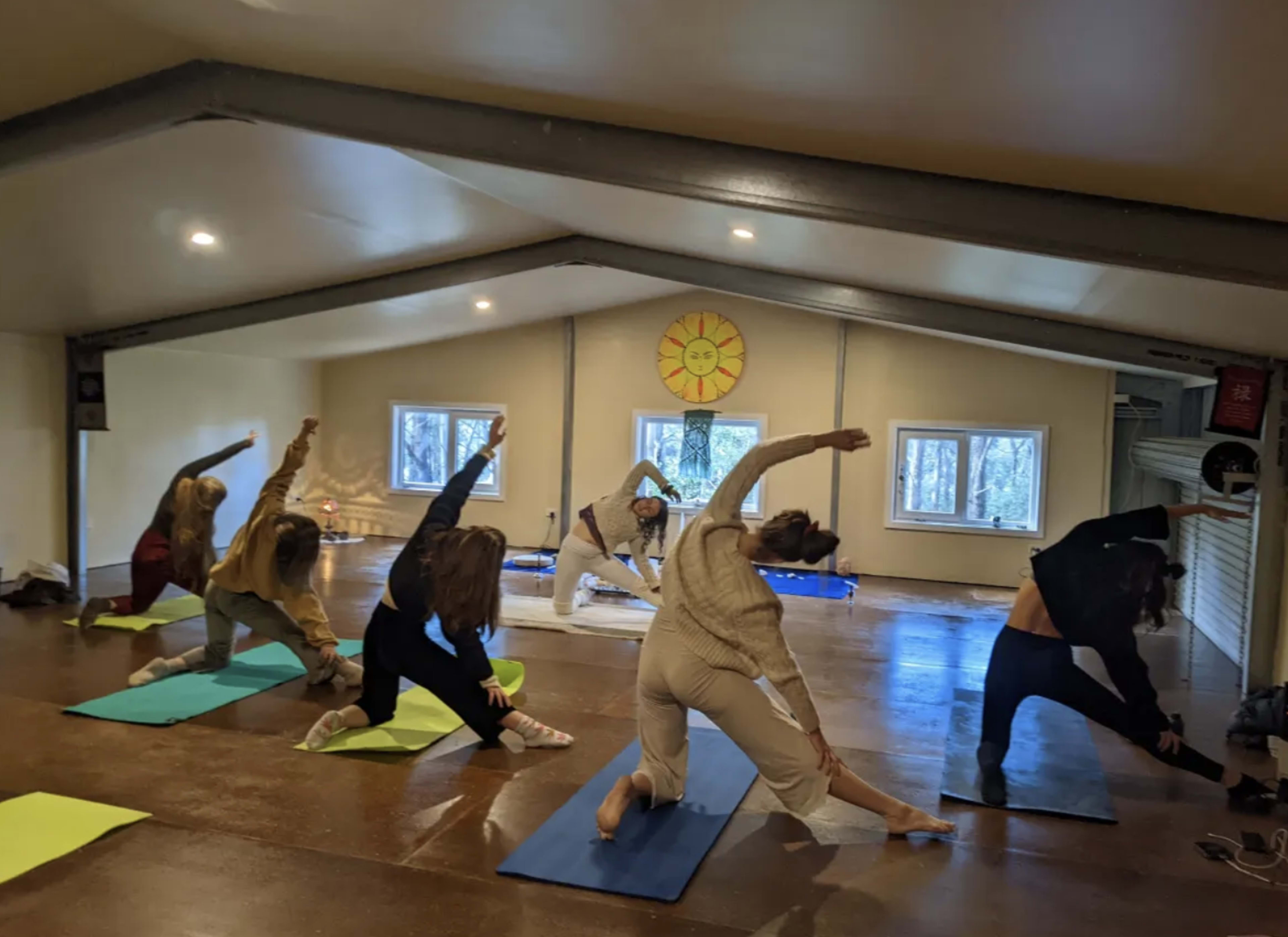 A group of six individuals are practicing yoga on mats in a spacious, well-lit studio.