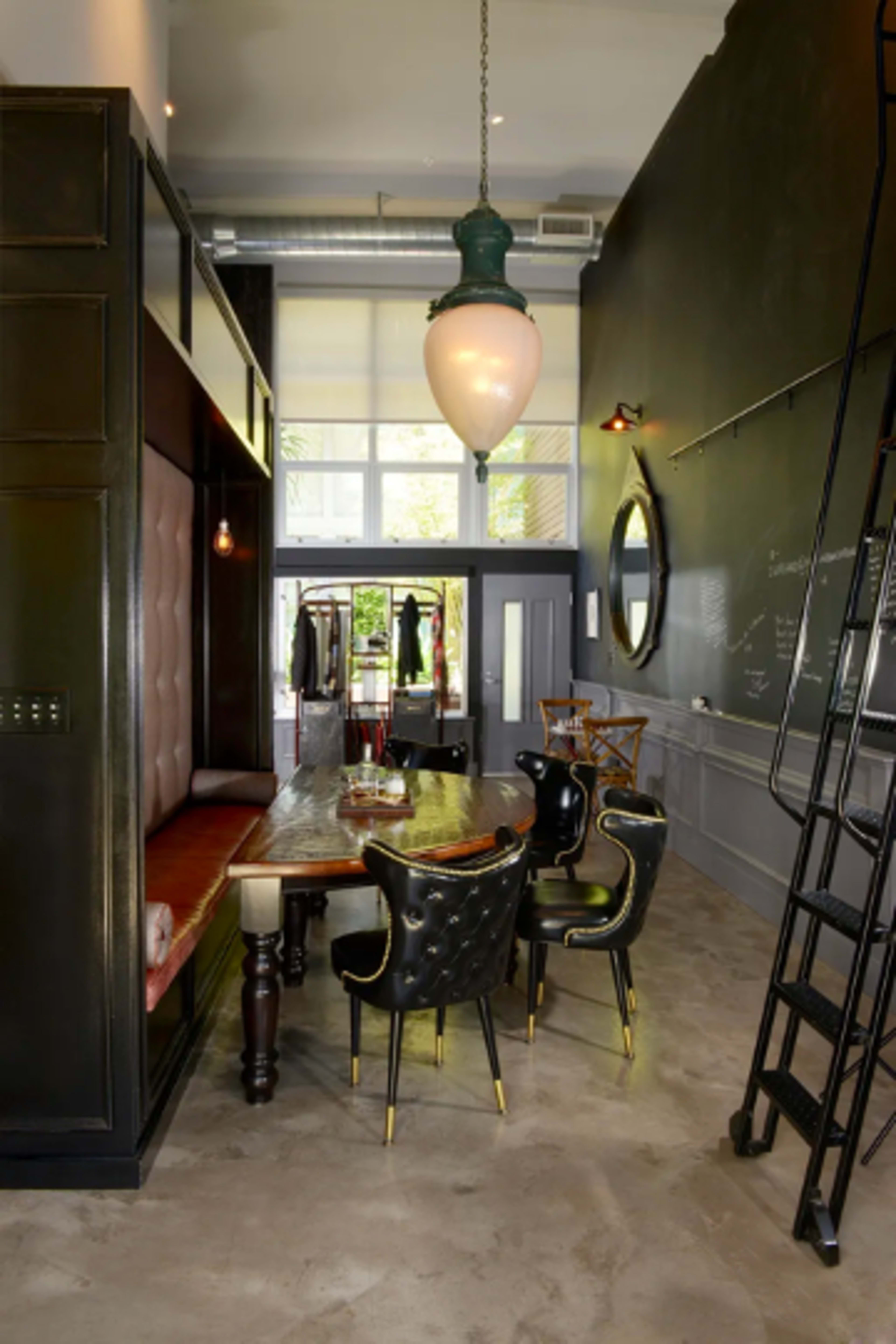 A modern dining area featuring a long wooden table surrounded by black upholstered chairs, with a large pendant light hanging above.