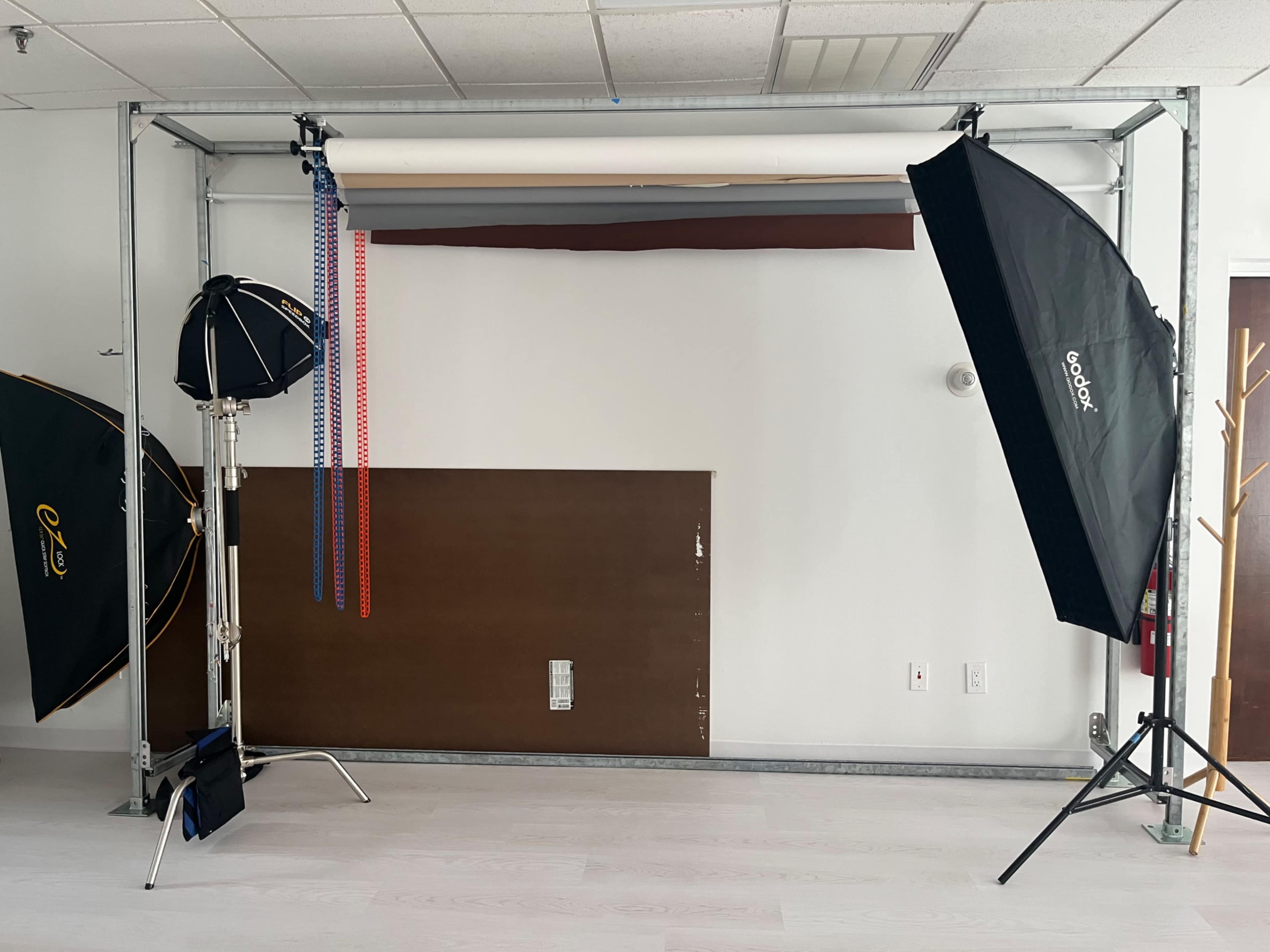 The image shows a photography setup with a backdrop support frame, studio lights, and various accessories arranged in a room.