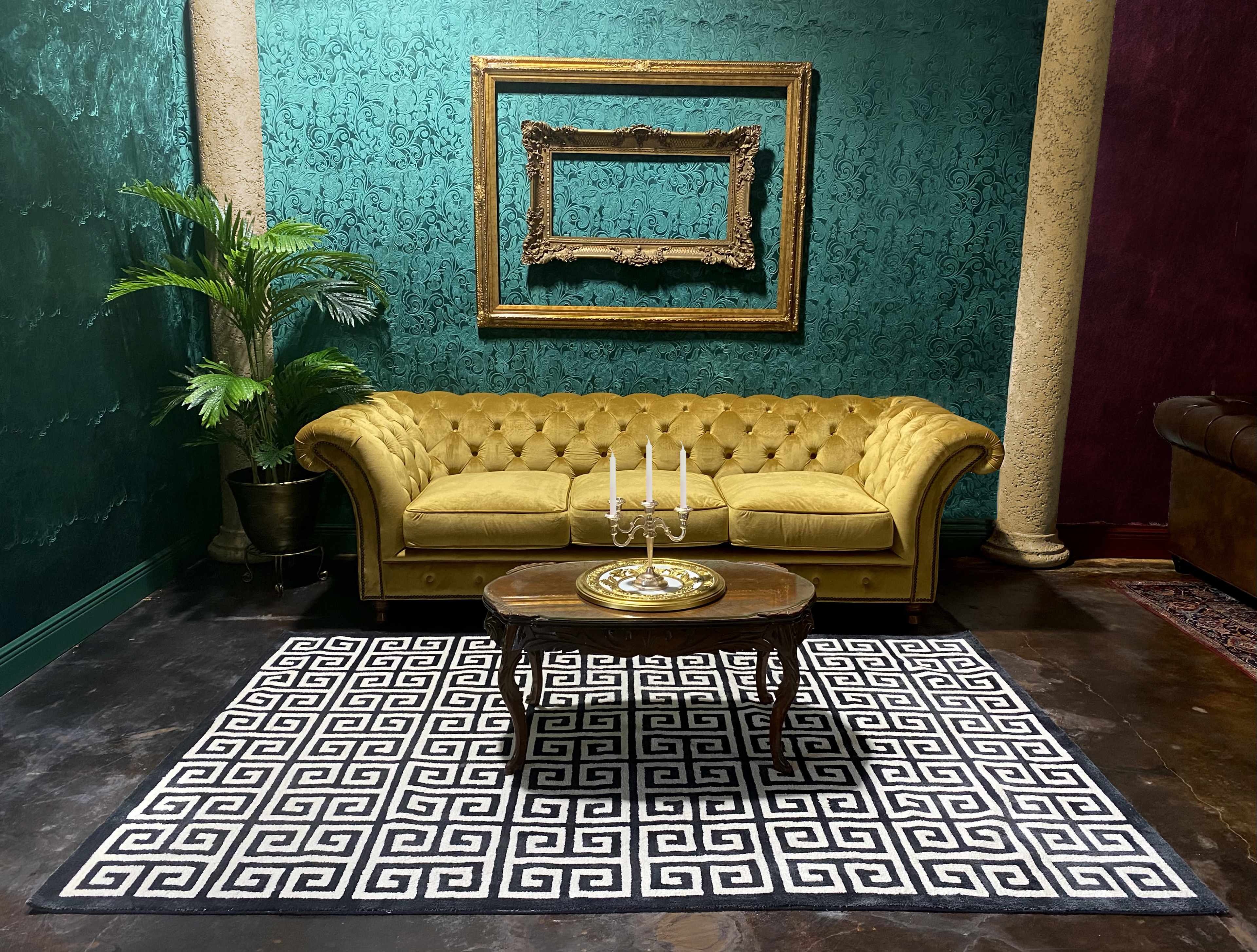 A vintage-style room featuring a yellow tufted couch, a round wooden coffee table with a decorative centerpiece, and a patterned black and white rug against a green and textured wall.