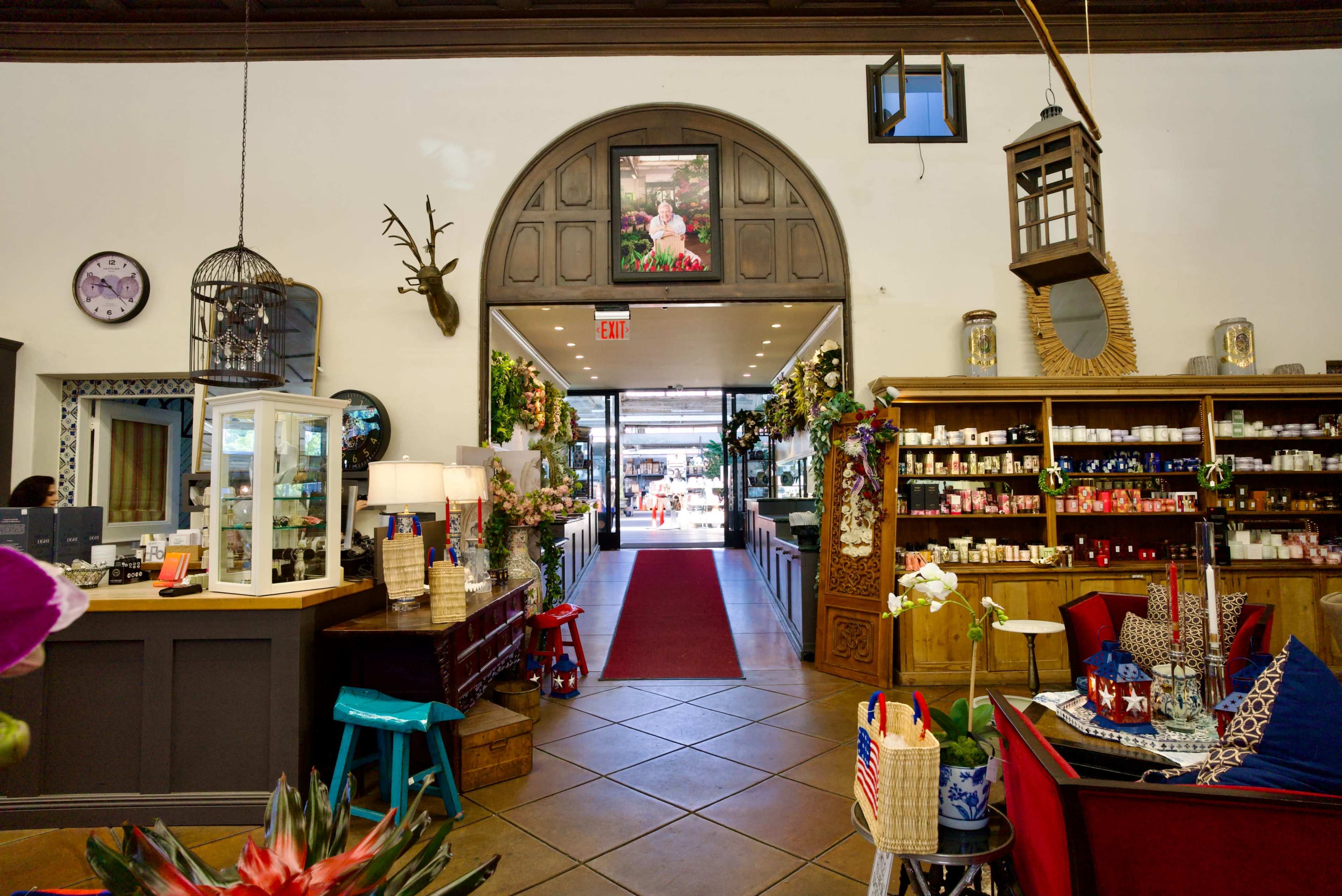 The image shows the interior of a shop featuring a wide entrance, decorative shelves filled with various products, and a red carpet leading outside.