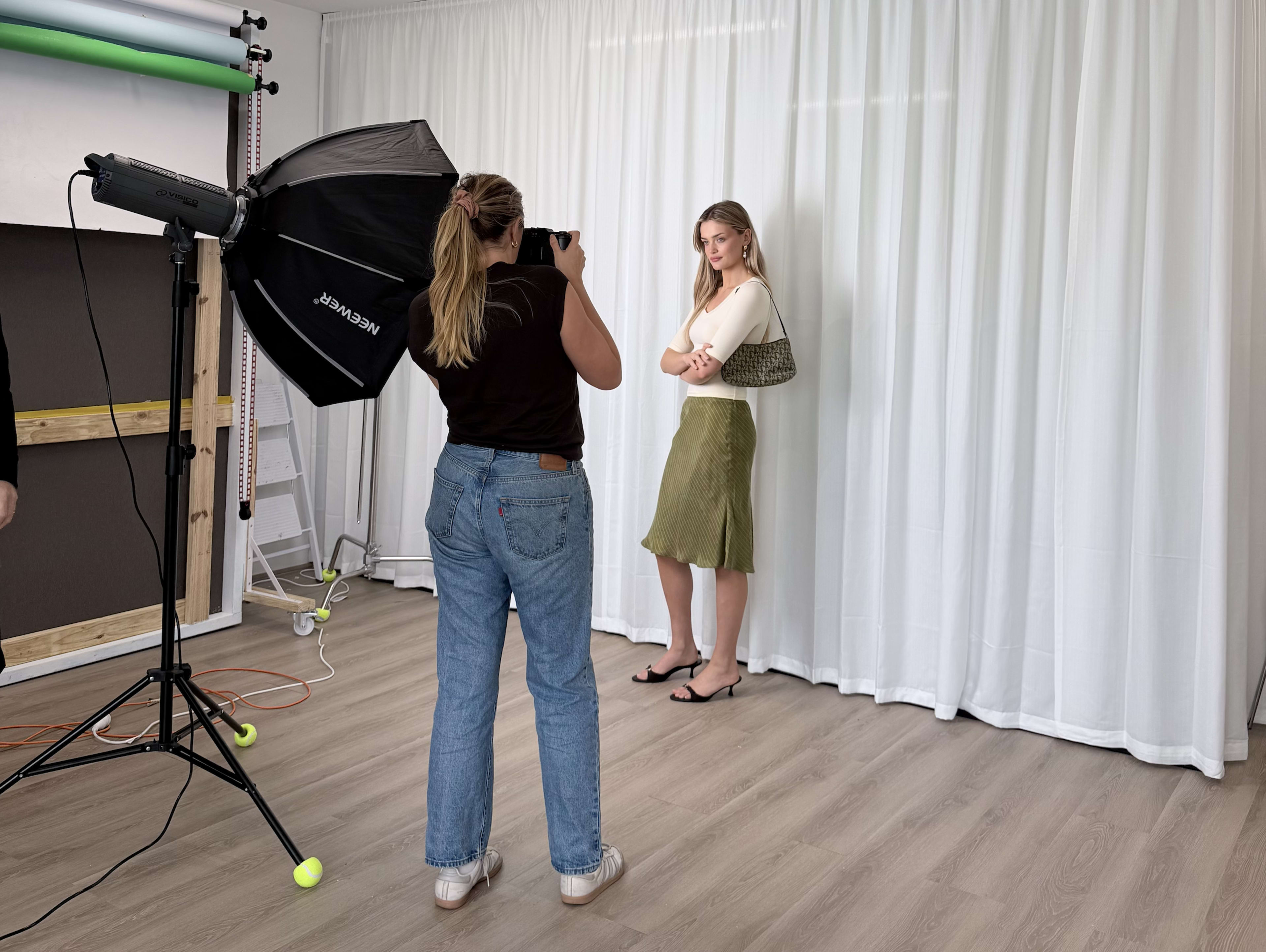 A photographer captures a model posing against a white backdrop in a well-lit studio.