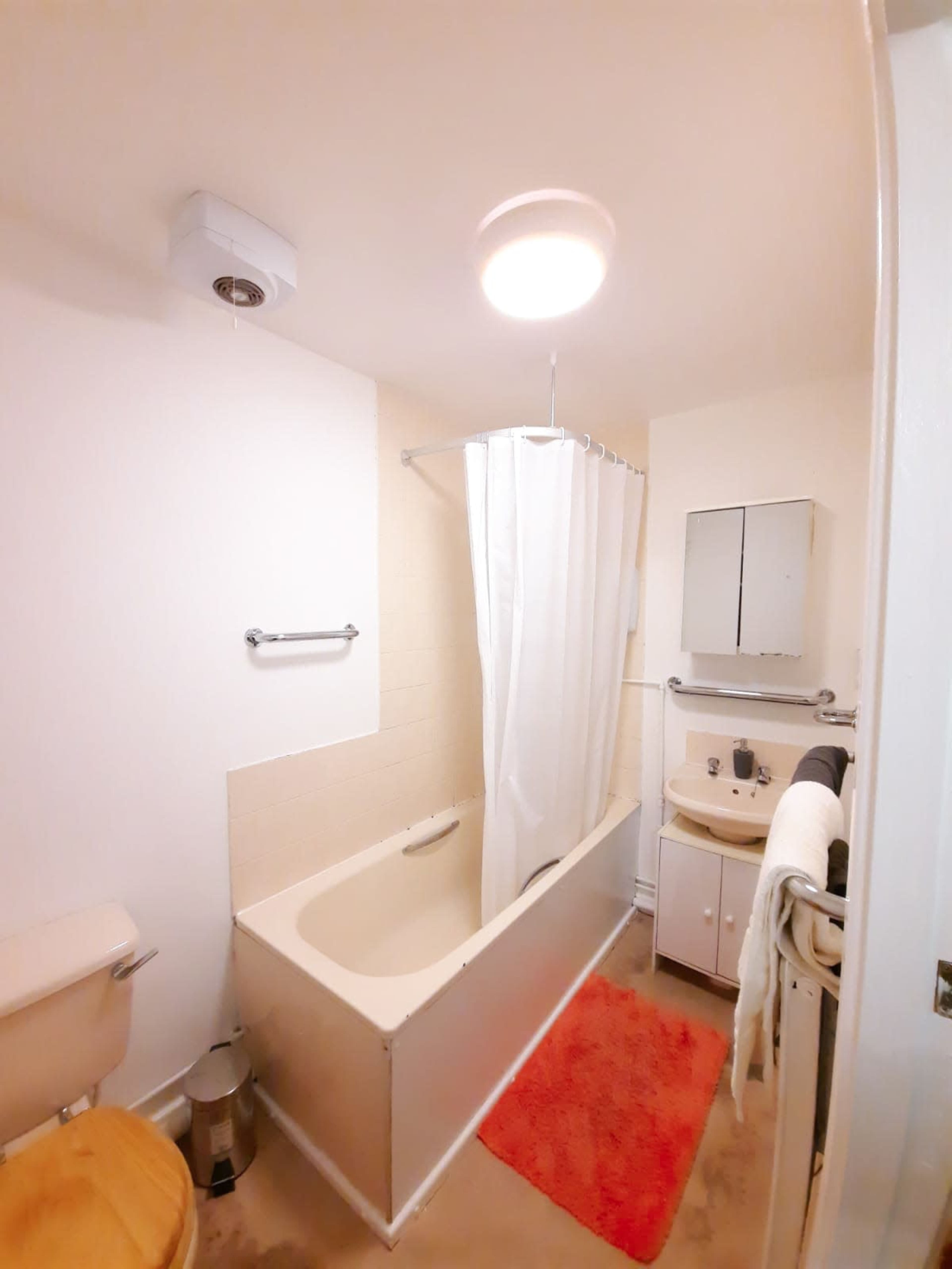 A bathroom with a bathtub, a shower curtain, a toilet, a sink with a cabinet, and a bright ceiling light.