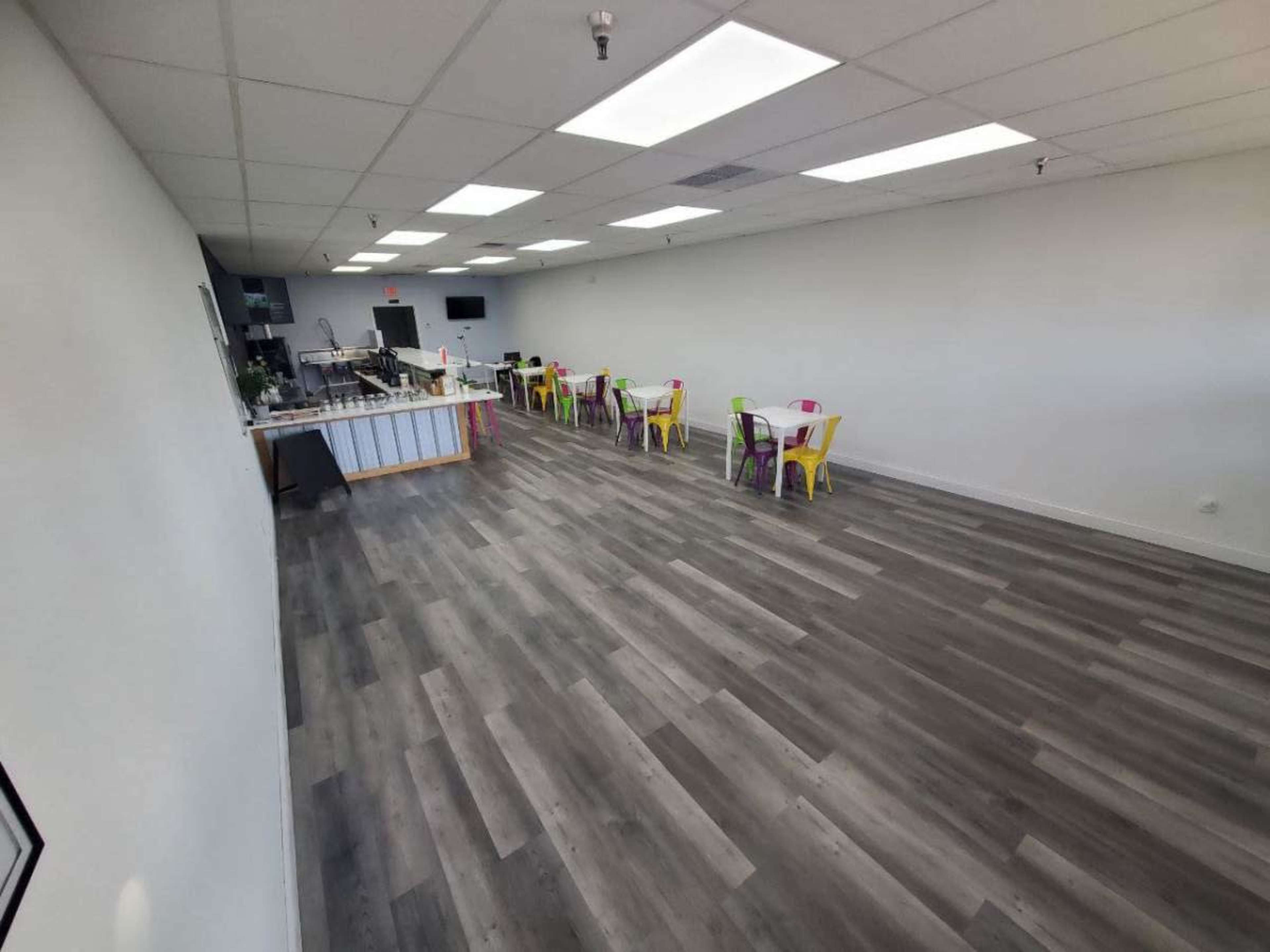 A spacious, brightly illuminated room with a row of colorful chairs and tables along one side.