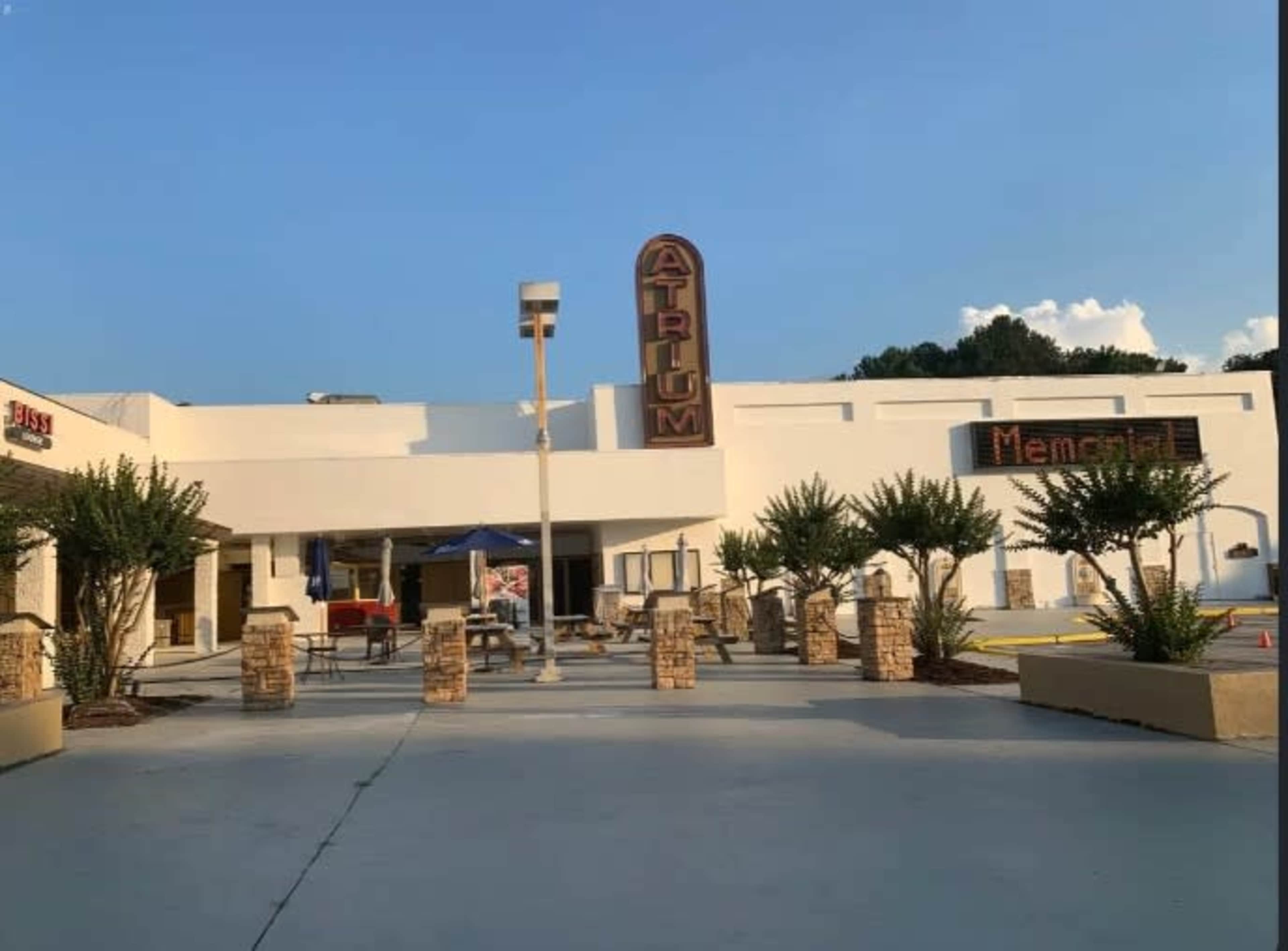 The image shows a building with a sign labeled "Atrium" prominently displayed, surrounded by landscaped planters and a clear blue sky.
