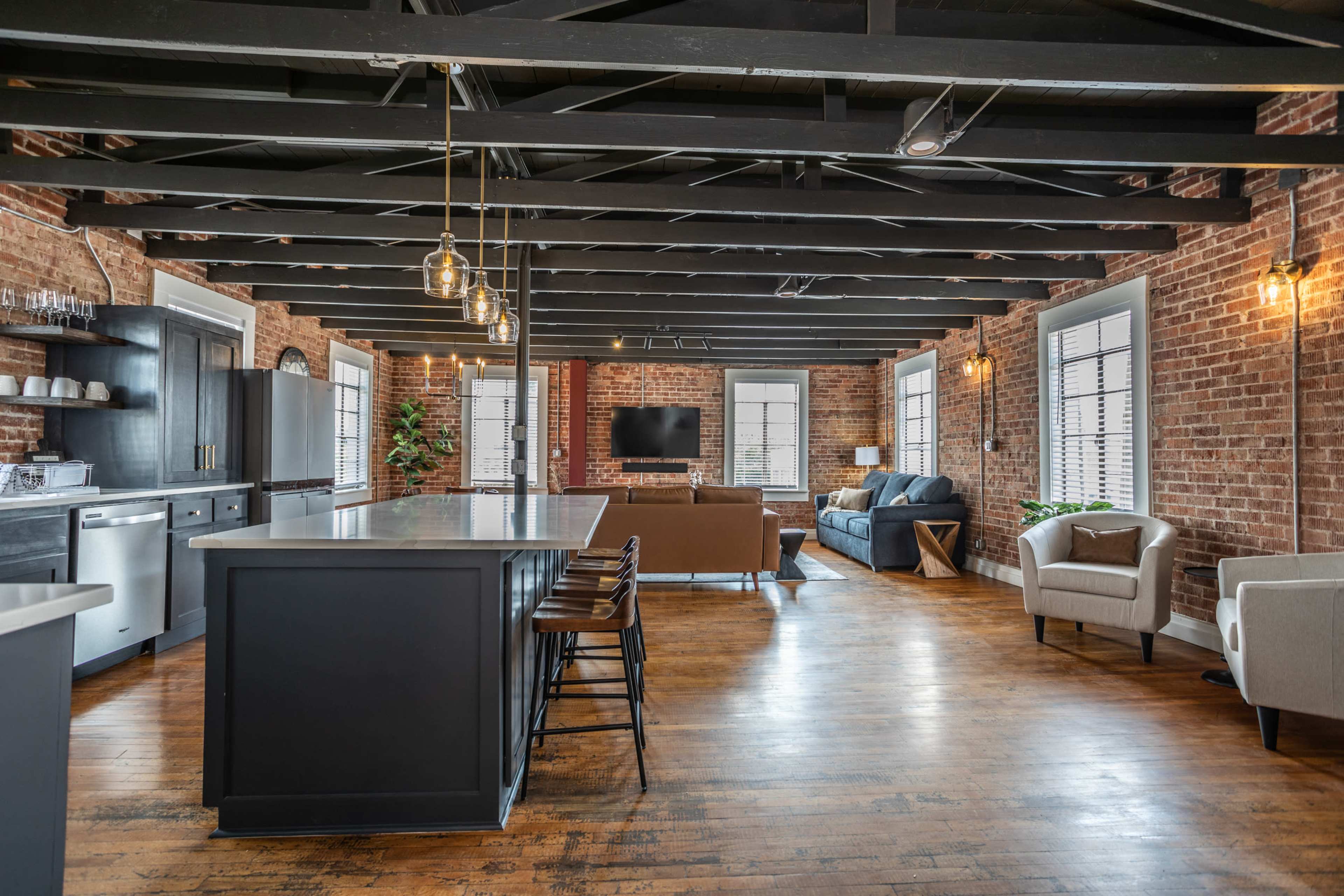 A spacious, modern loft apartment with exposed brick walls, a large kitchen island, and comfortable seating areas.
