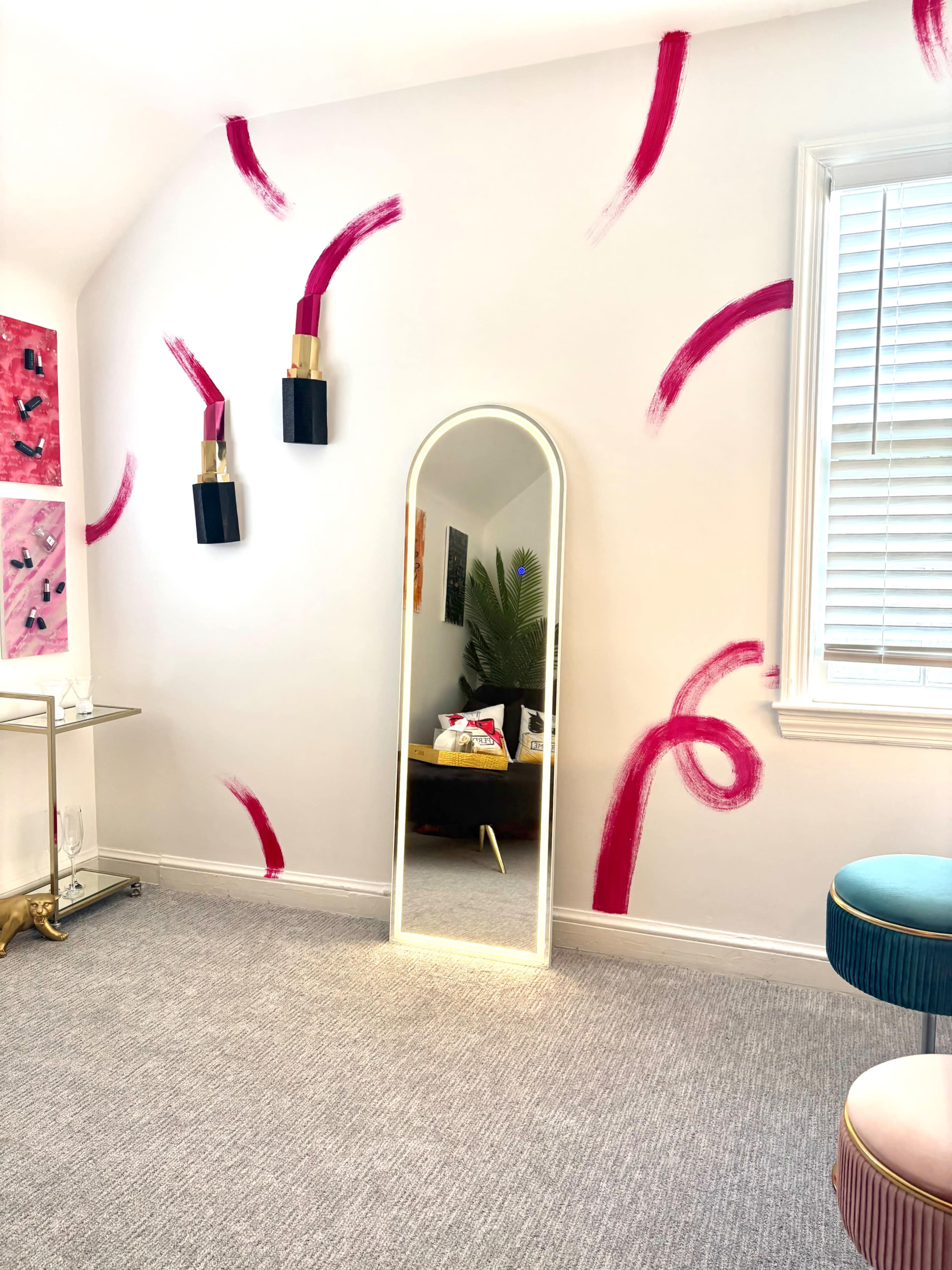 The image shows a room with a large mirror, two wall-mounted light fixtures, and abstract pink brushstroke designs on the walls.
