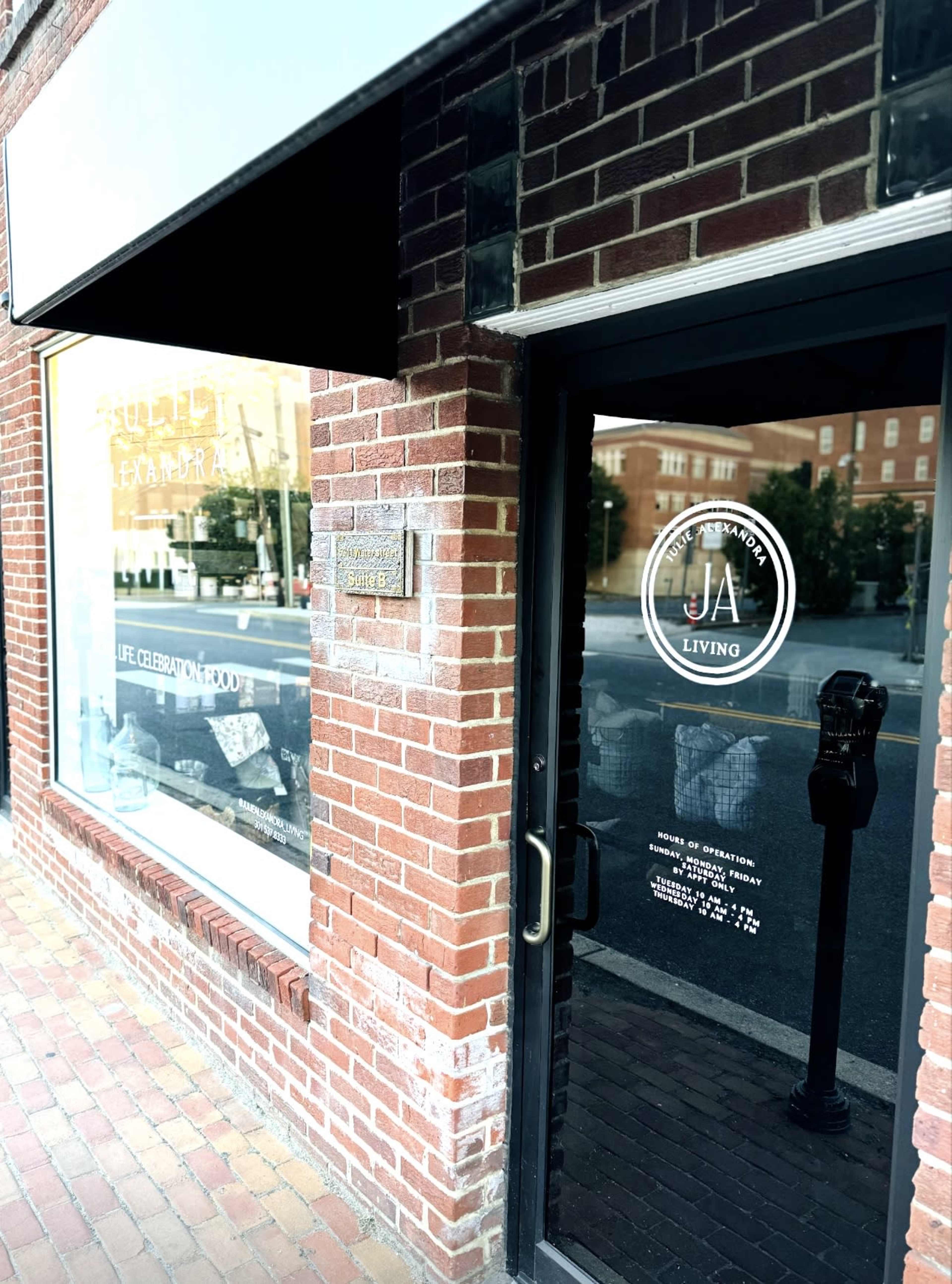 A storefront with a glass door featuring a circular logo labeled "JA LIVING" and a visible parking meter outside on a brick sidewalk.