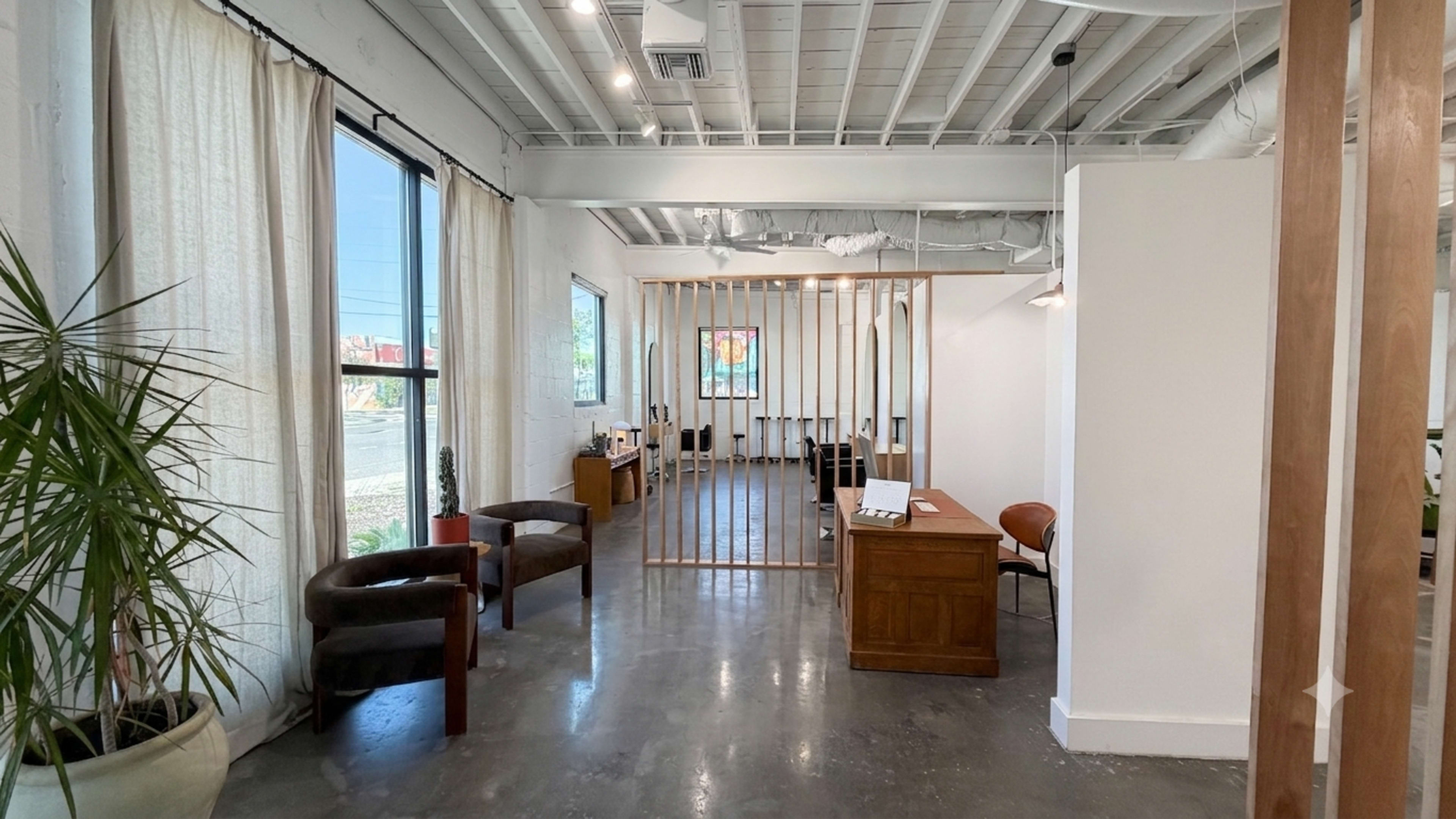 The image shows a modern office interior featuring a reception area with a wooden partition, chairs, and natural light coming through large windows.