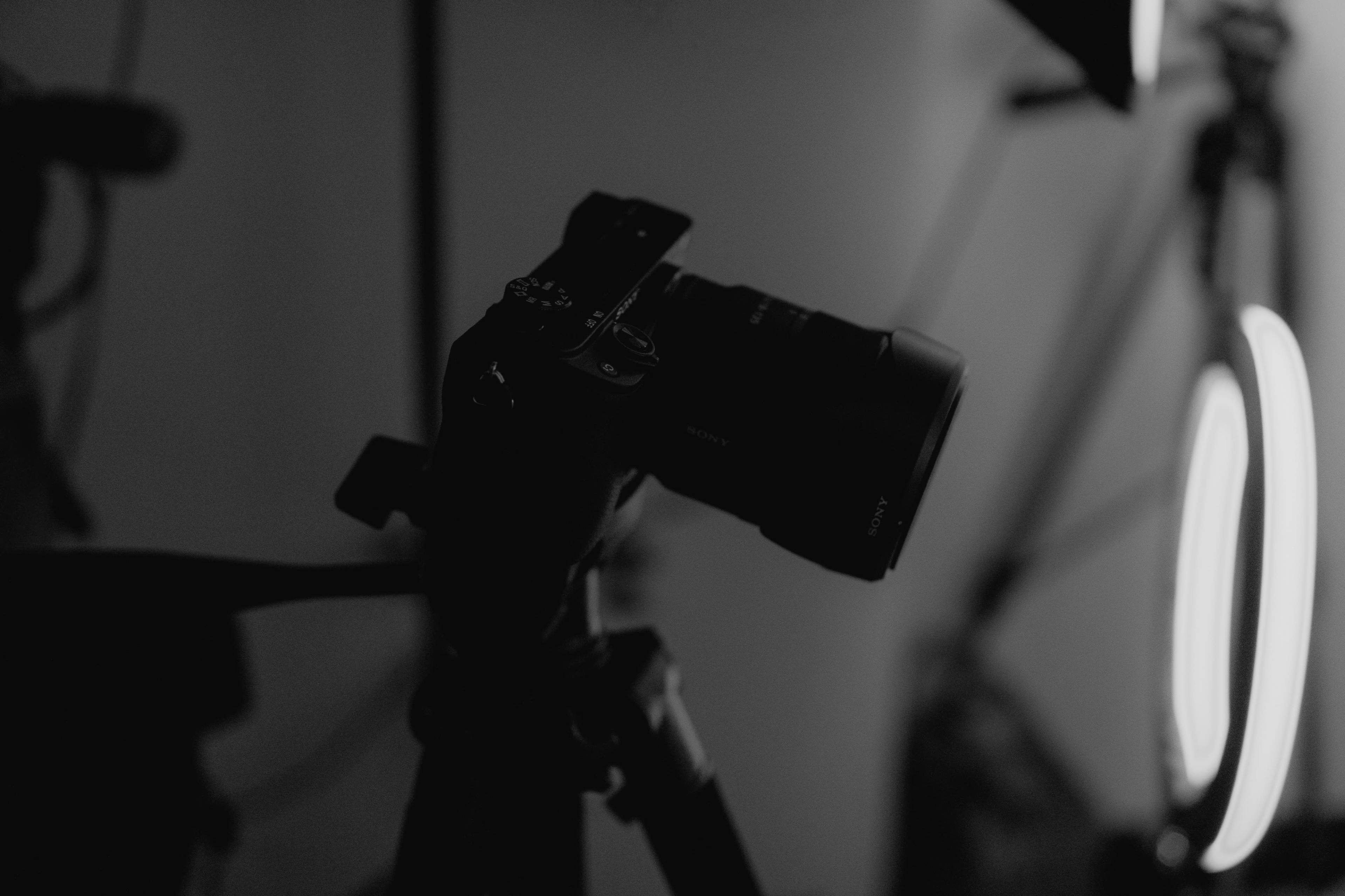 A camera is mounted on a tripod, positioned in front of bright circular lighting.