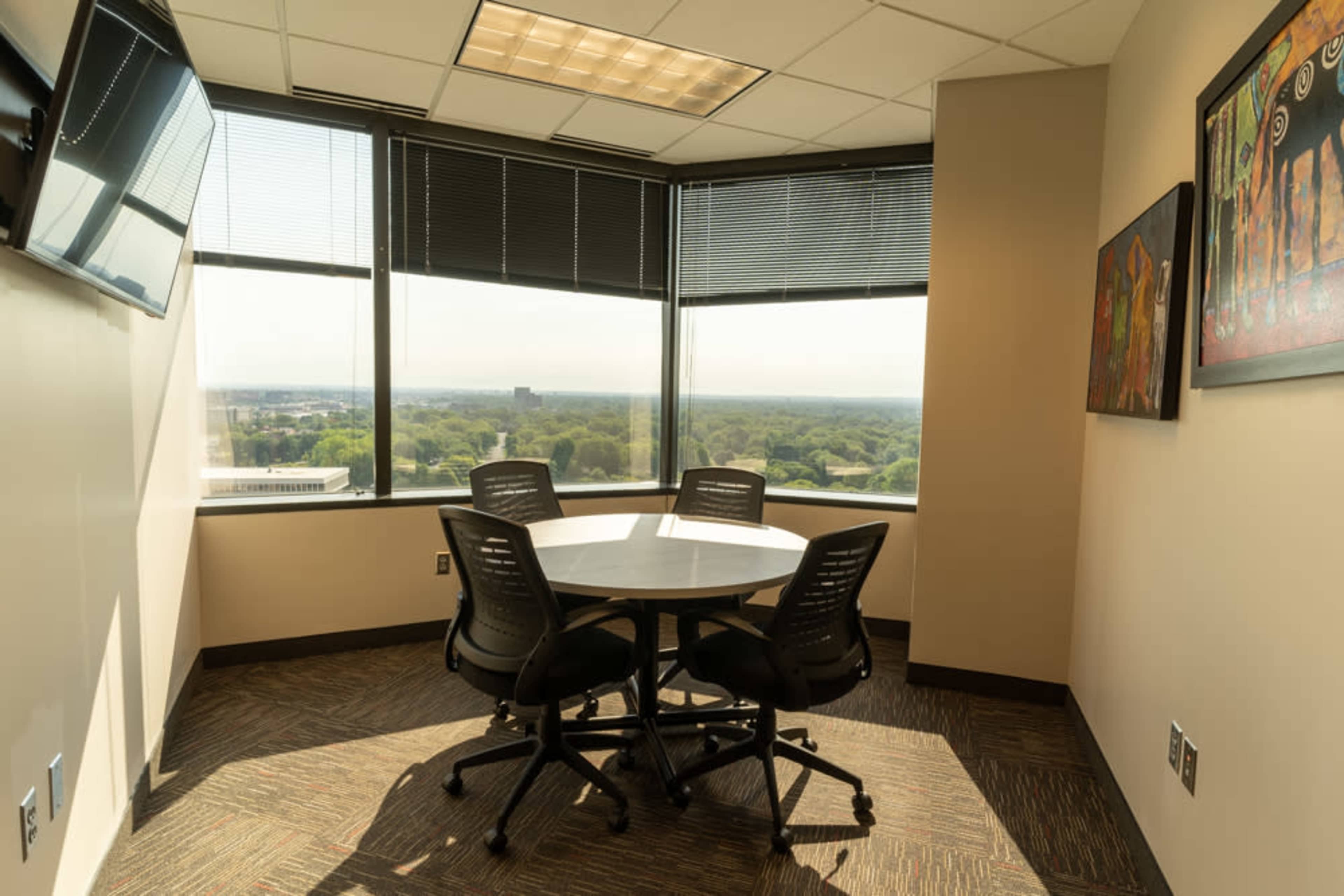 A small conference room with a round table and four chairs is situated in a corner, featuring large windows that offer a view of the surrounding landscape.