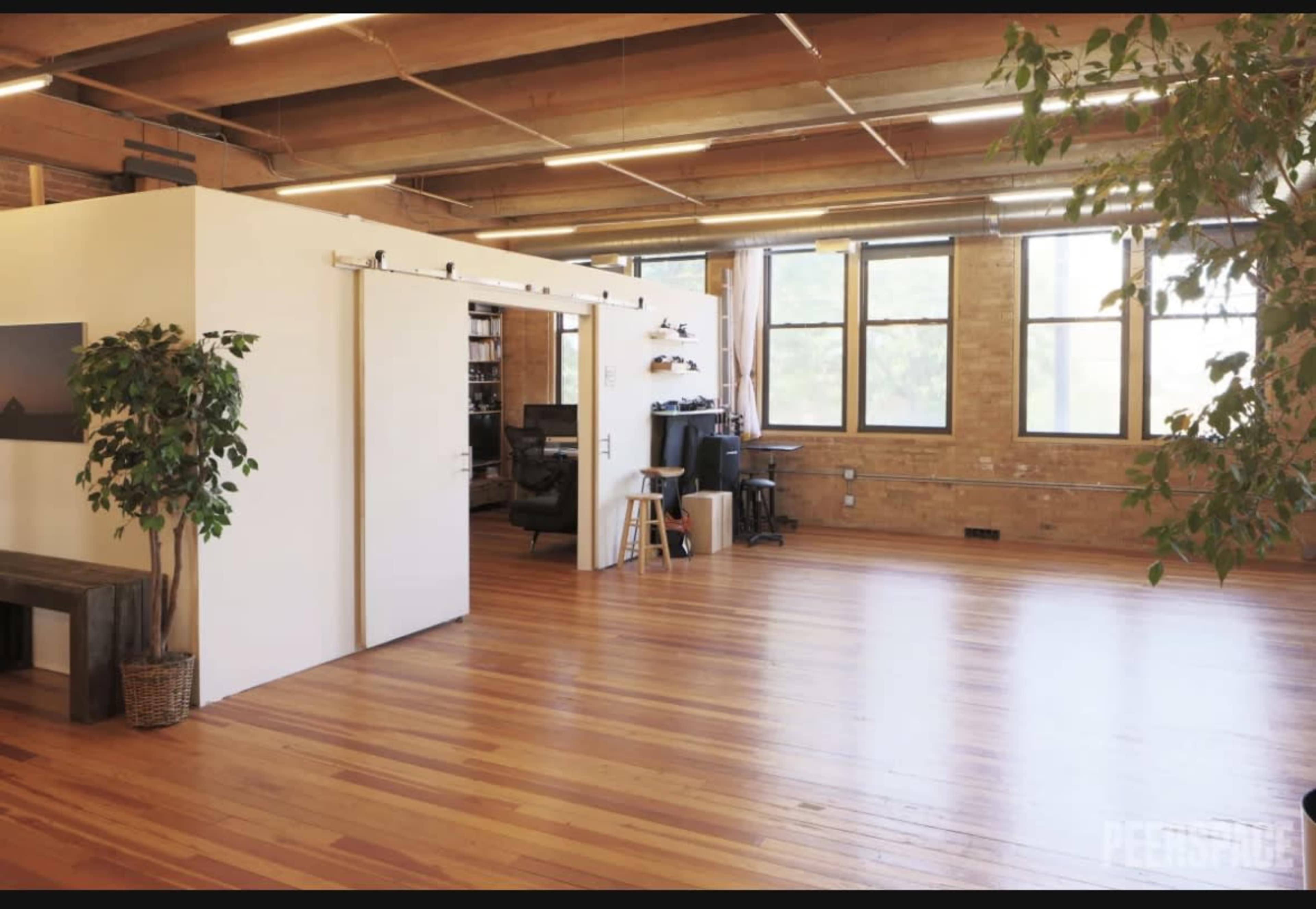 A spacious, well-lit room with polished wooden floors, featuring a partitioned area and large windows.