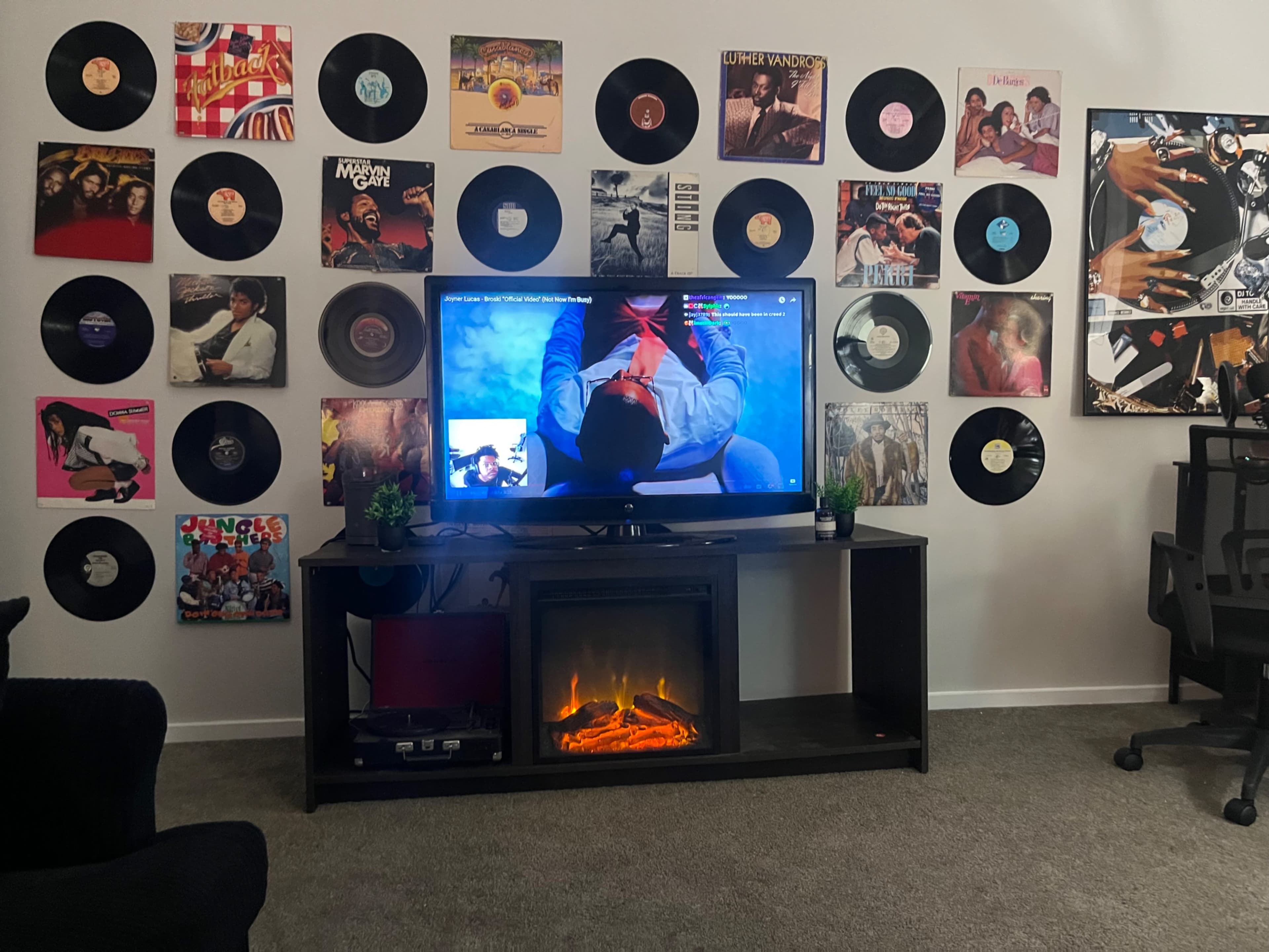 The image shows a living room with a television mounted in front of a wall decorated with vinyl records and a faux fireplace beneath the TV.