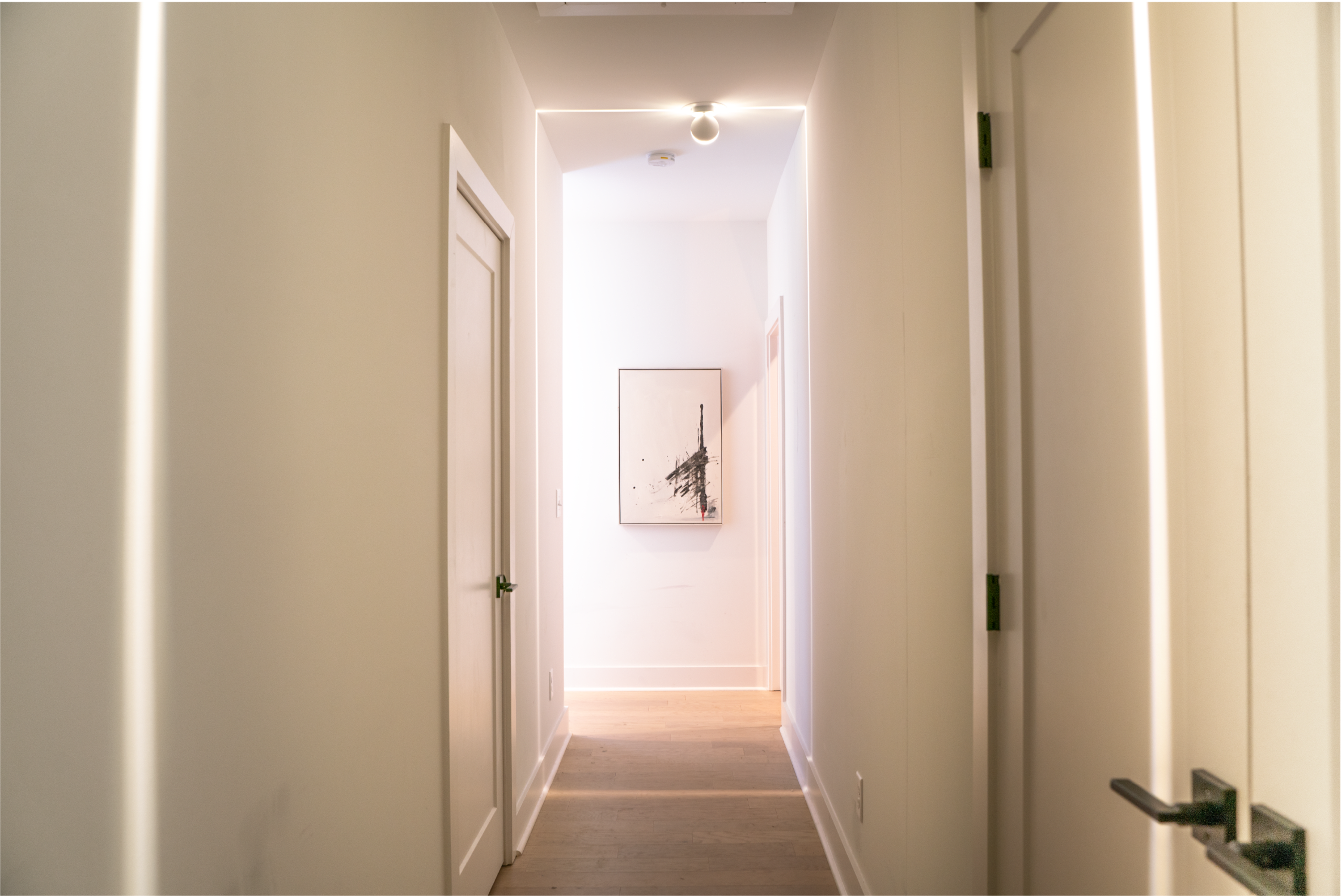 A narrow hallway with light-colored walls and a piece of artwork at the far end.